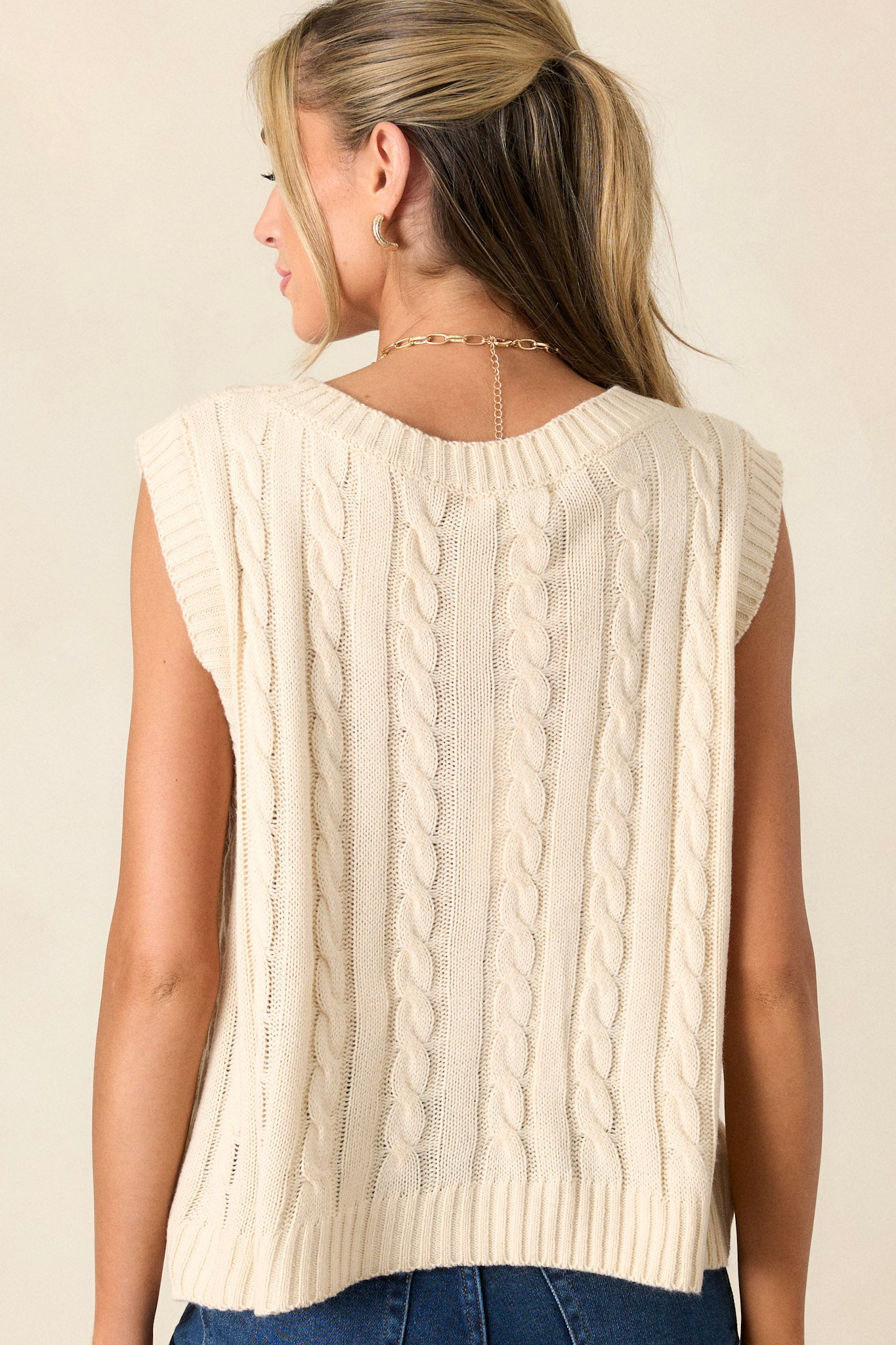 Back view of the sweater vest showing the smooth cable-knit design extending across the back and the structured ribbed waistline for a fitted appearance.