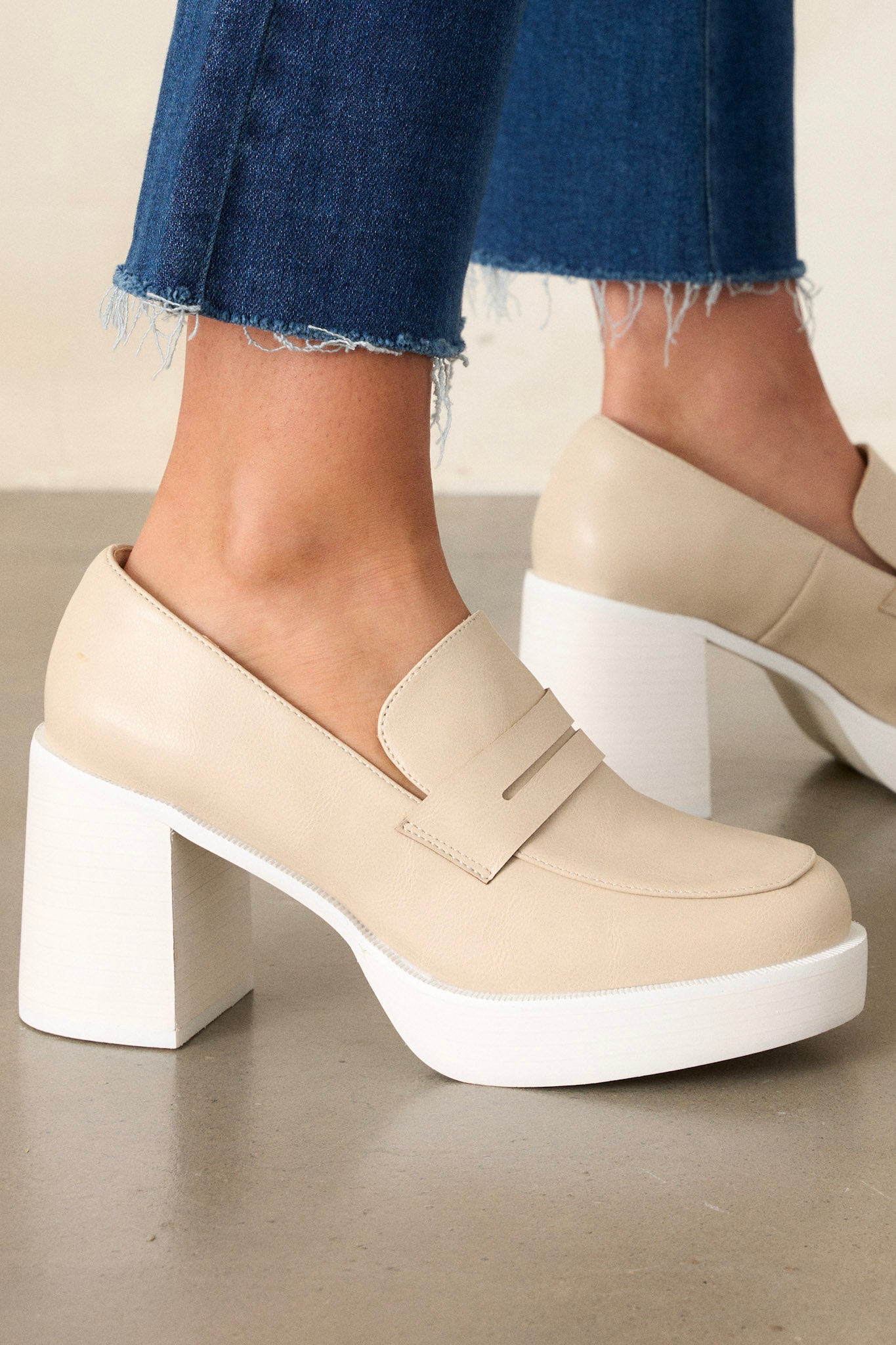 Close-up view of these beige loafers that feature a white platform sole, faux leather, and a block heel.