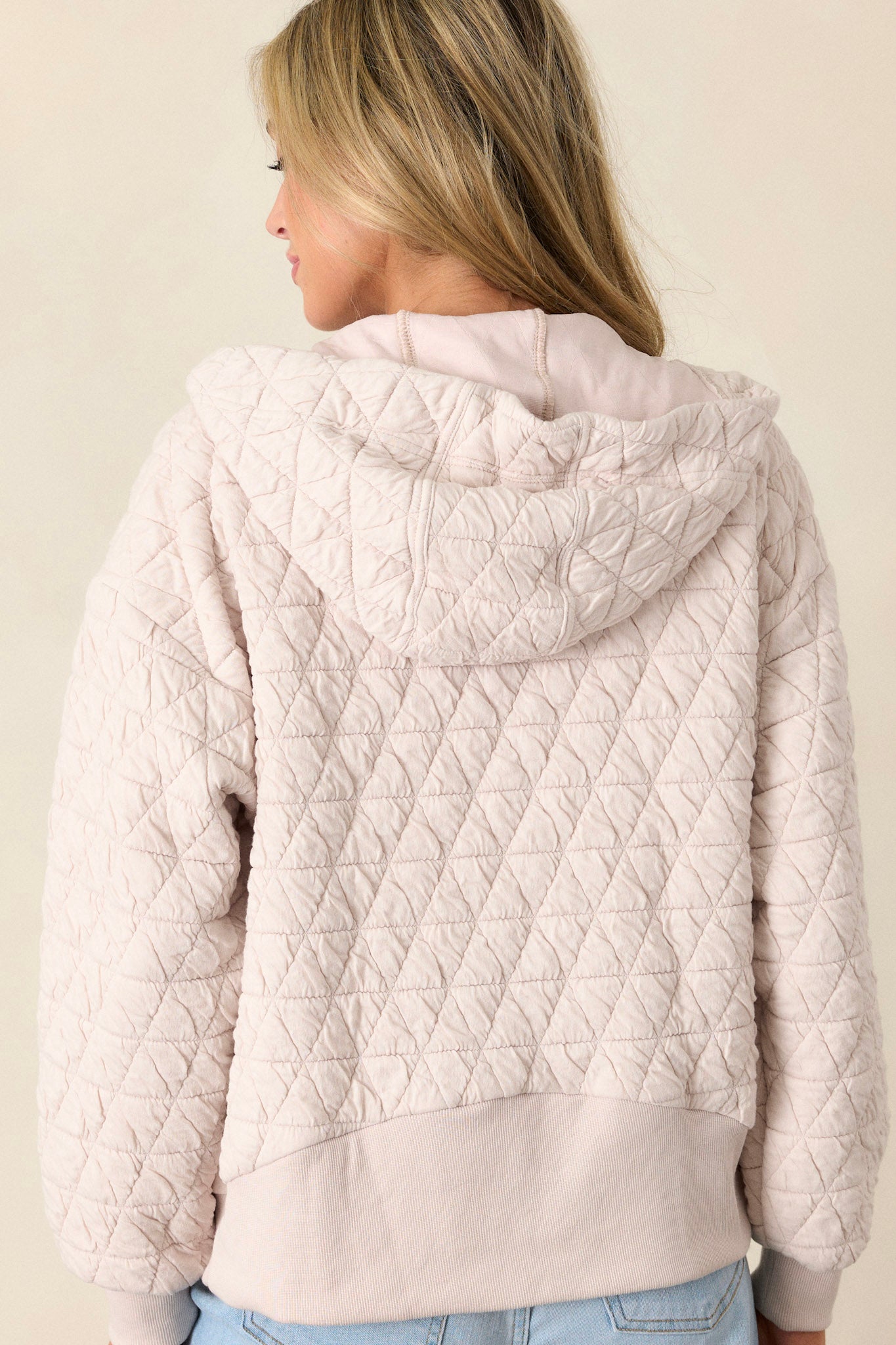 Back view of the ivory quilted jacket highlighting the thick hem, quilted design, and cuffed long sleeves.