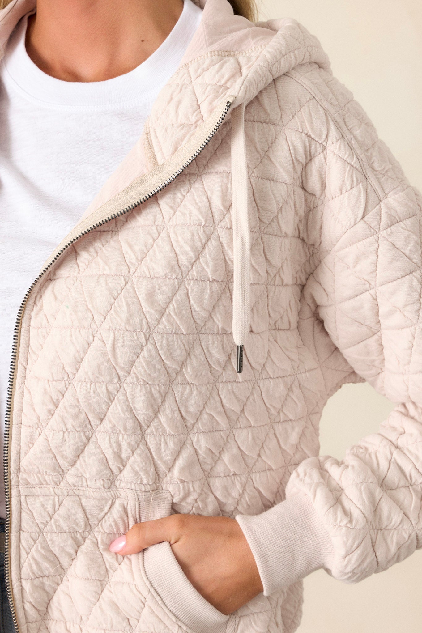 Close-up of the ivory quilted jacket focusing on the high neckline, zipper closure, quilted texture, and the detailing on the thick hem and cuffed long sleeves.