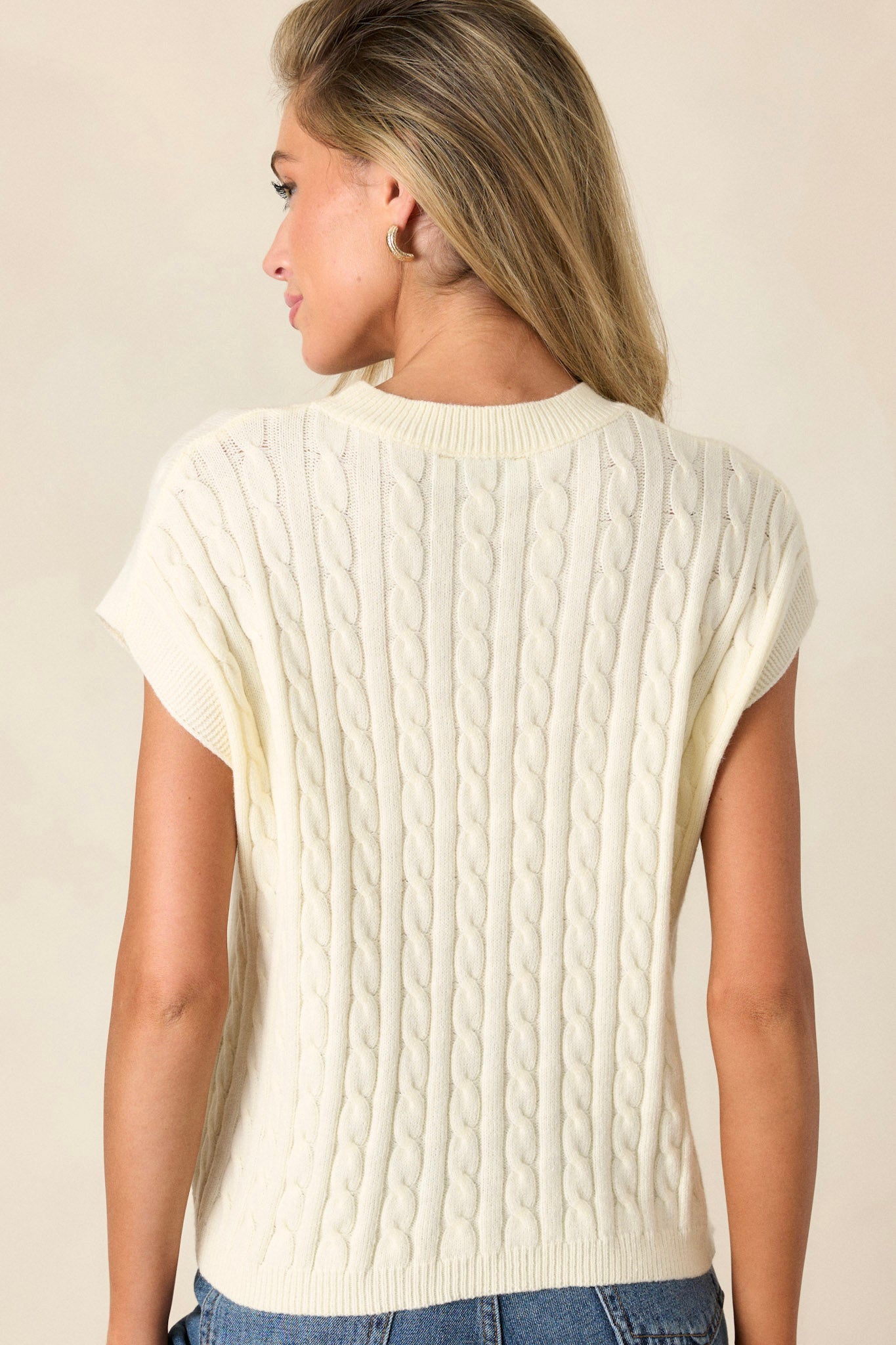 Back view of a white top highlighting the cable-knit pattern, ribbed neckline, and ribbed waistline.