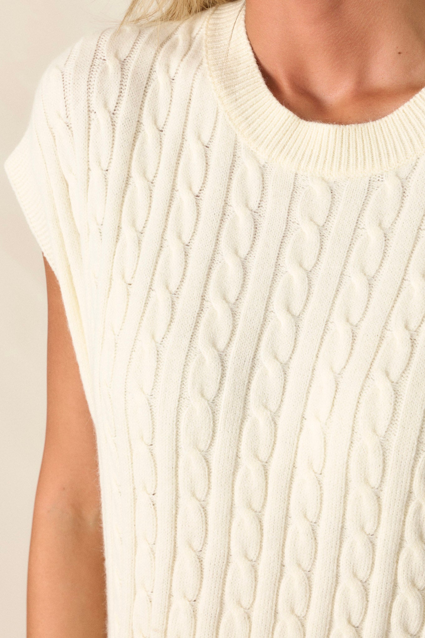 Close-up of the white top focusing on the cable-knit design, ribbed neckline, and texture of the ribbed waistline.