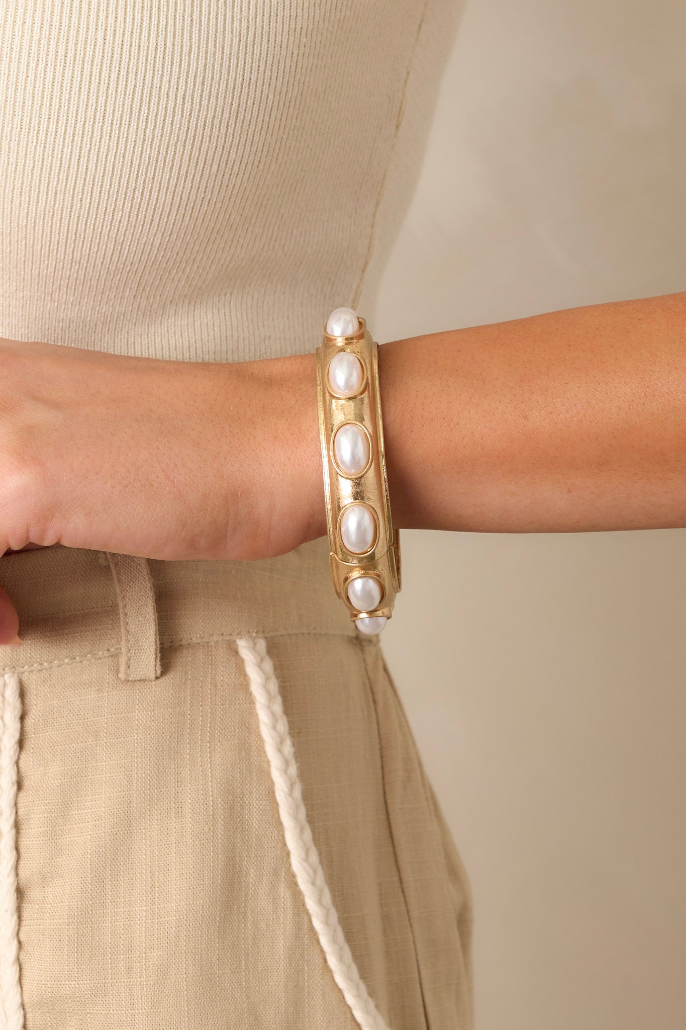 Close-up view of this gold bracelet featuring worn gold colored hardware, evenly spaced oval pearl embellishments, and an elastic band underneath.