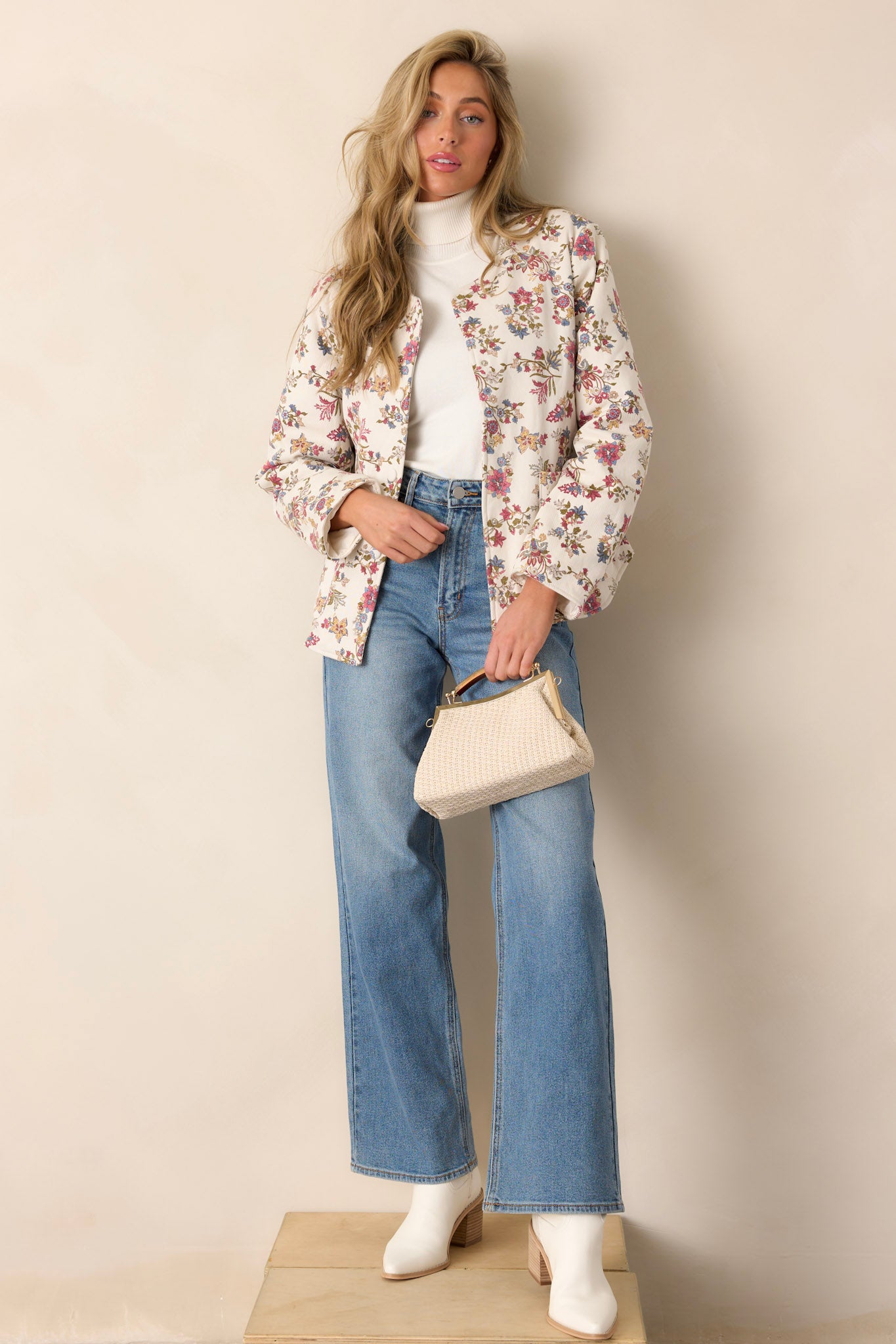 Full length view of an ivory floral jacket featuring a crew neckline, functional buttons down the front, two functional hip pockets, and a floral denim fabric