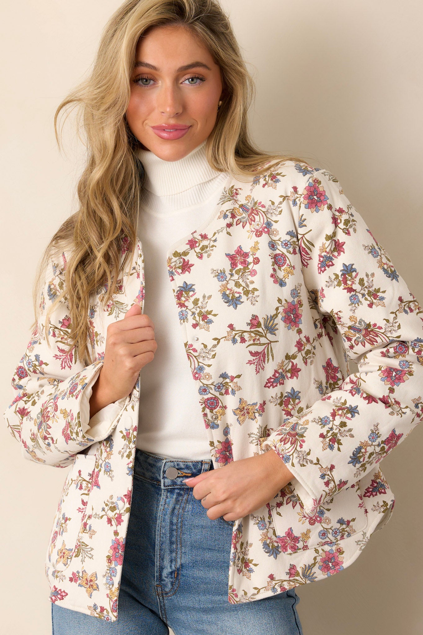 Front view of an ivory floral jacket featuring a crew neckline, functional buttons down the front, two functional hip pockets, and a floral denim fabric