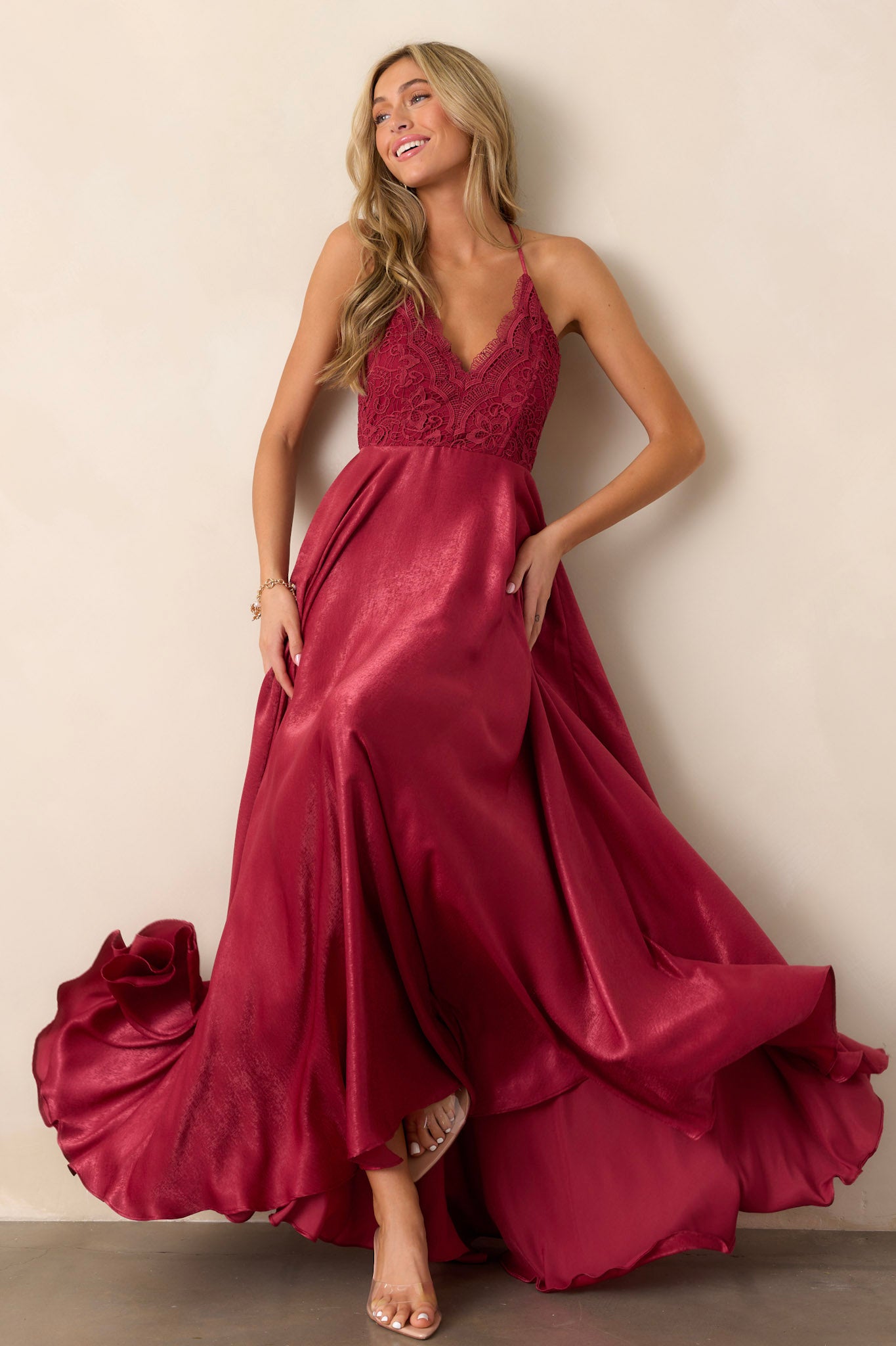 Full length view of a model wearing the cranberry dress, featuring a v-neckline, lace detailing on the bust, an open back, and a back zipper.