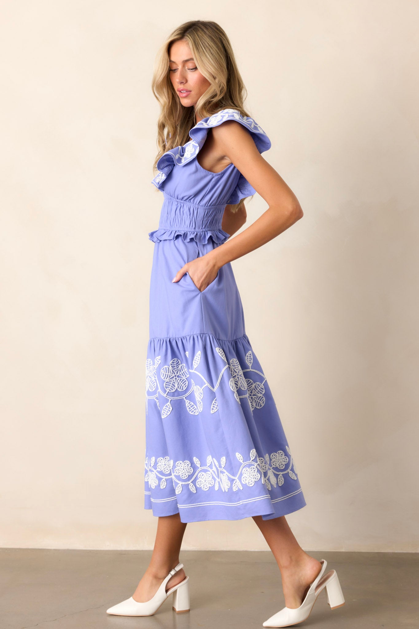 Side view of the periwinkle dress showcasing the plunging v-neckline, smocked waist, and the short flutter sleeves, with a glimpse of the embroidered detailing and functional hip pockets