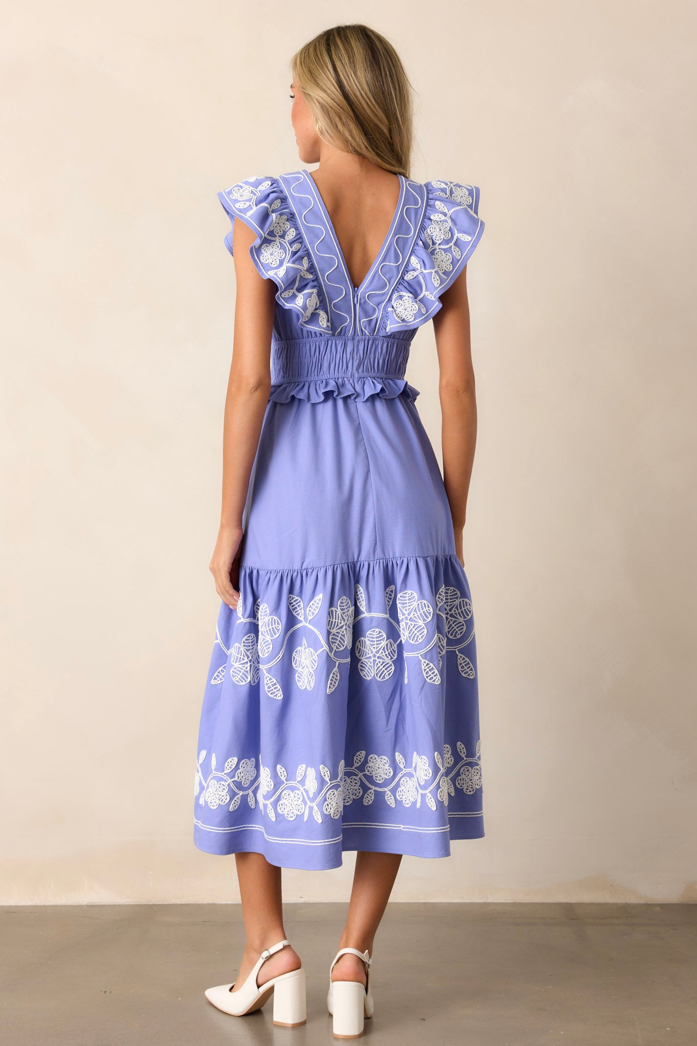 Back view of the periwinkle dress highlighting the smocked waist, the discrete back zipper, and the flow of the short flutter sleeves, with embroidered detailing visible across the fabric.