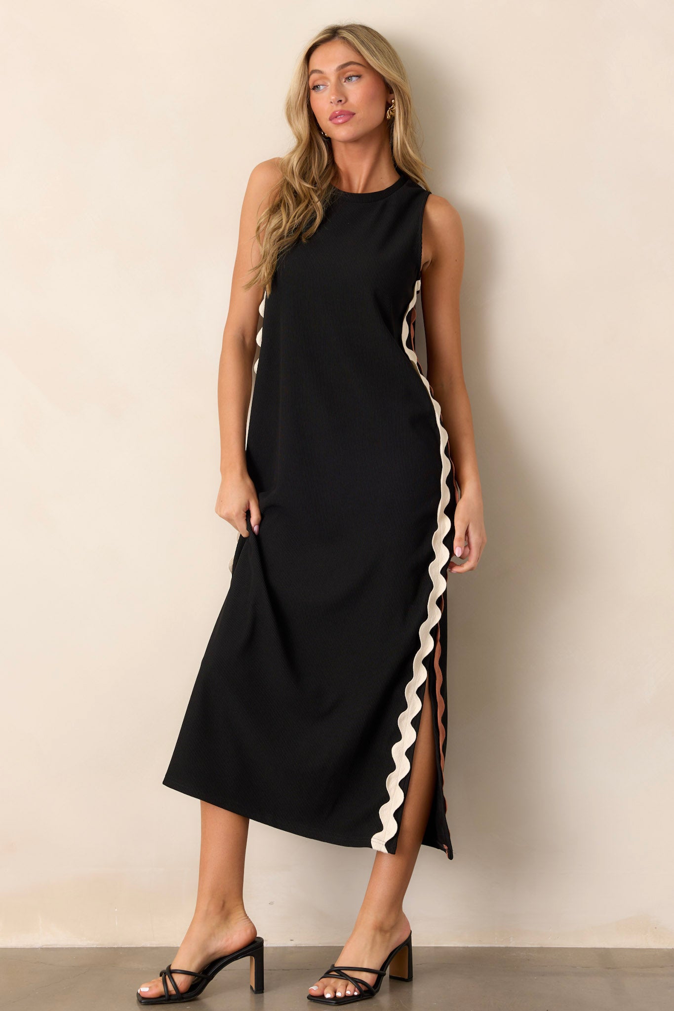 Front angled view of the black midi dress featuring a crew neckline, ribbed material, two-toned ricrac side detailing, side slits, and a sleeveless design