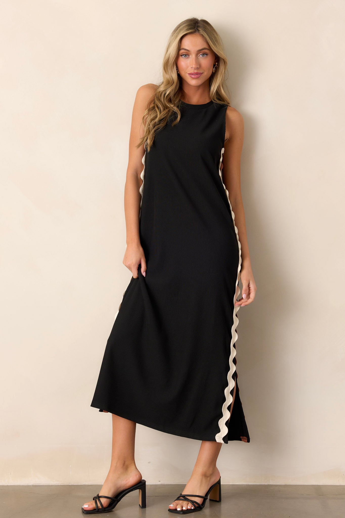 Front view of a black midi dress featuring a crew neckline, ribbed material, two-toned ricrac side detailing, side slits, and a sleeveless design.