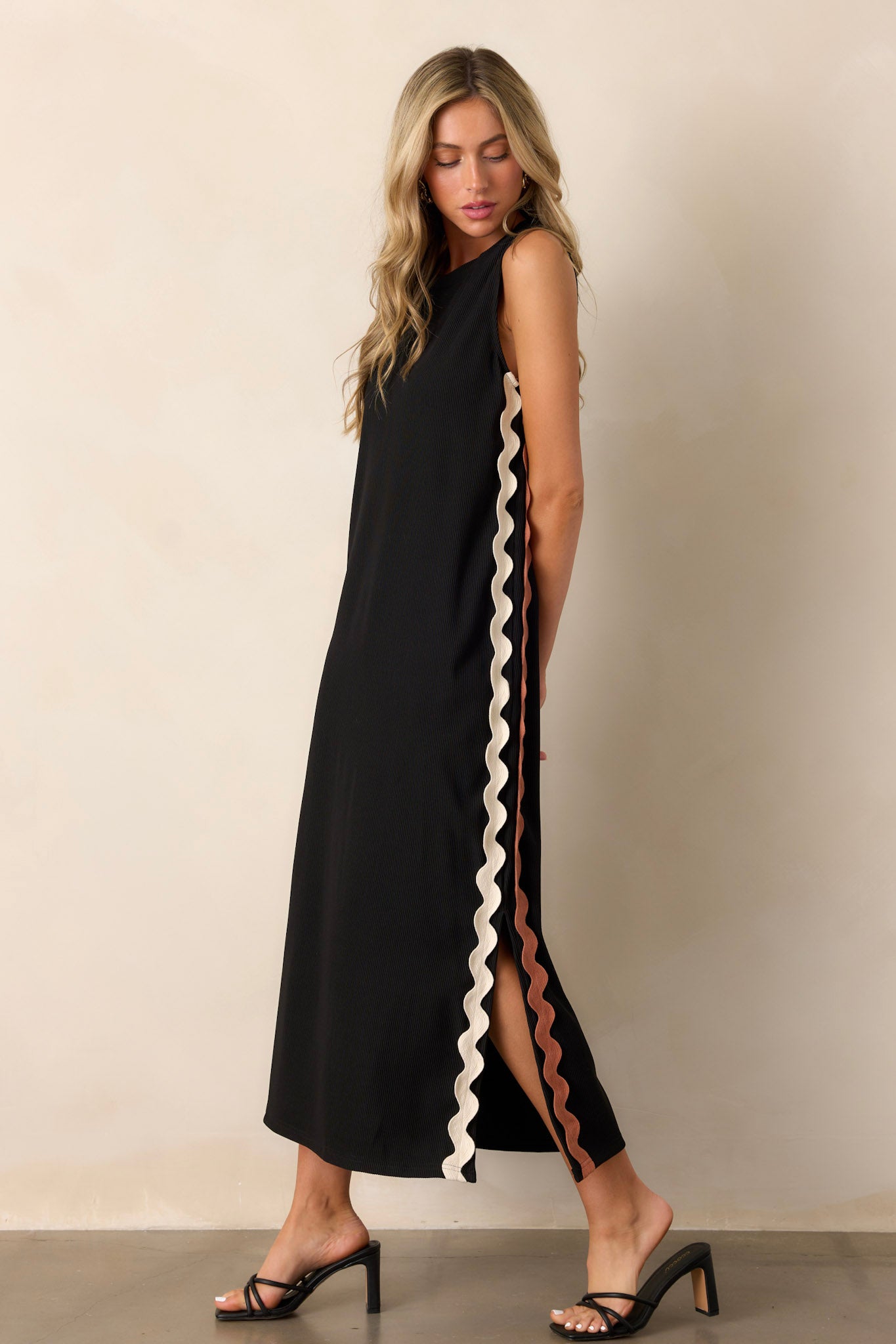 Side view of the black midi dress showcasing the ribbed material, two-toned ricrac side detailing, side slits, and sleeveless design.