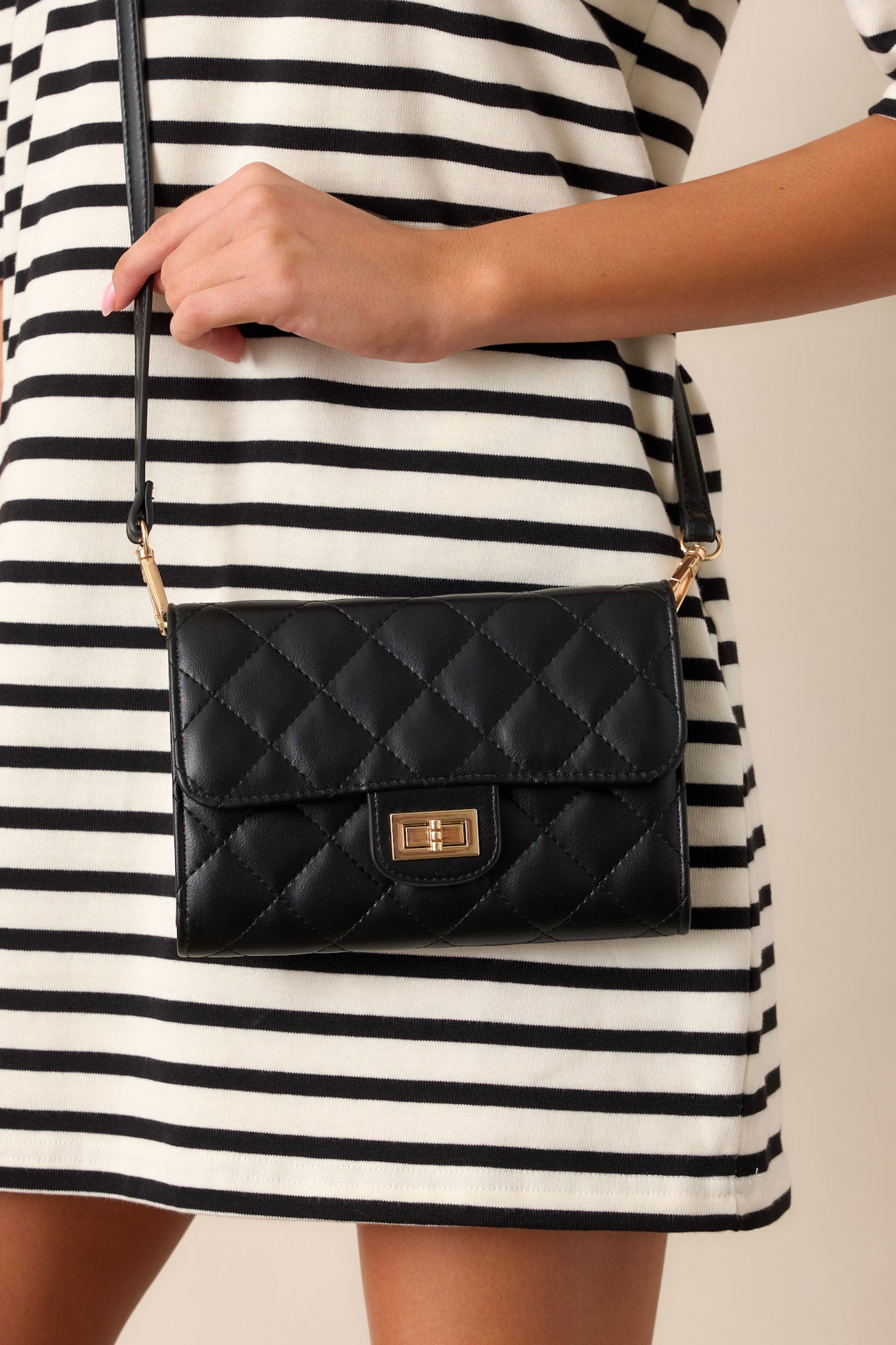 Hanging view of this black bag featuring gold hardware, a quilted design, turn lock closure, a zipper pocket inside, and a detachable chain shoulder strap.