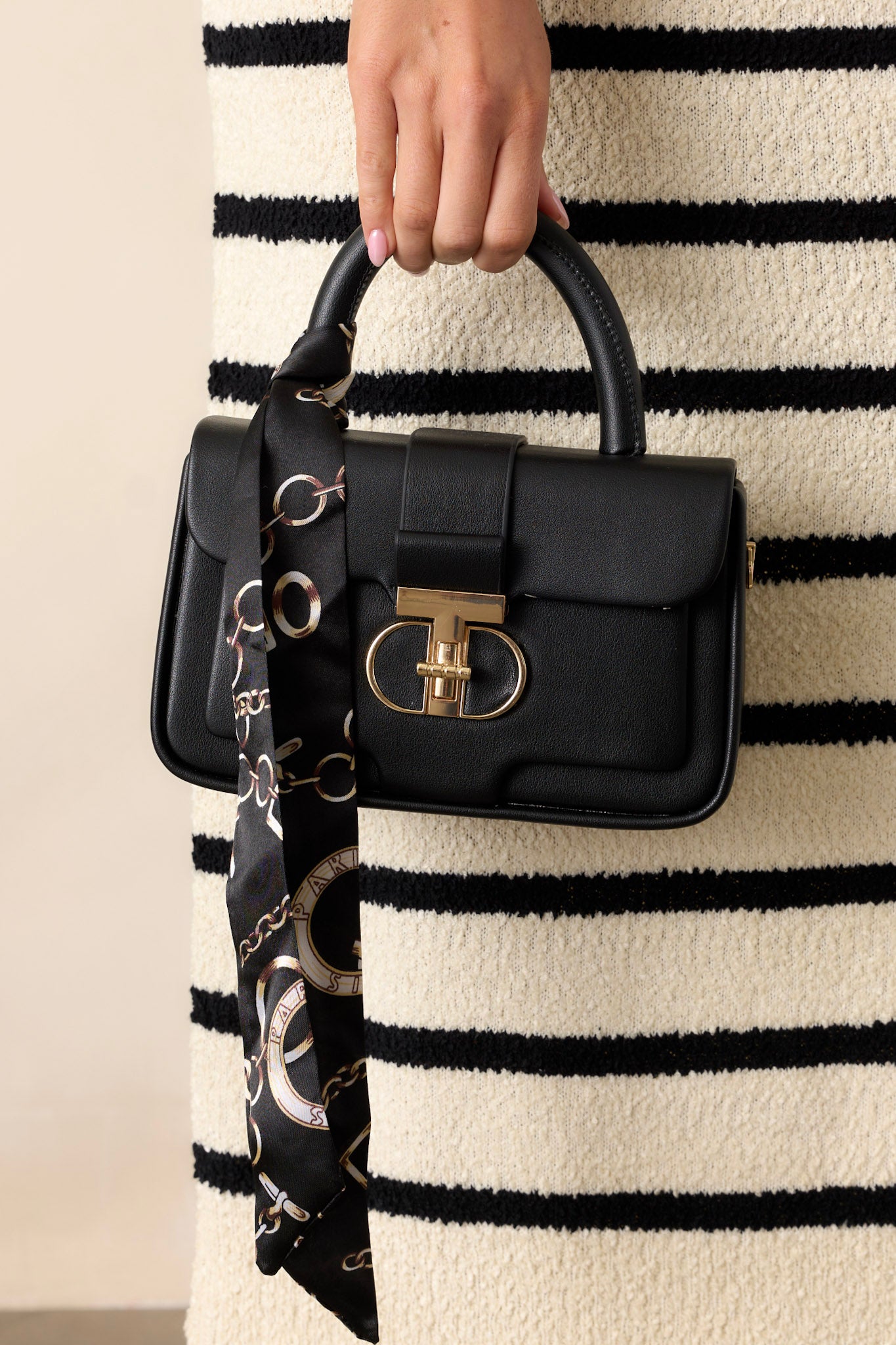 This black handbag features a gold accent turn closure, a built in pocket, a matching mini wallet and gold accent side loops for exchangeable straps.