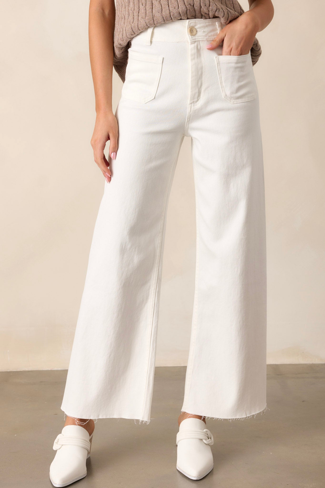 Front view of ivory pants featuring a high waisted design, a button & zipper closure, belt loops, functional front & back pockets, a wide leg design, and a raw hemline