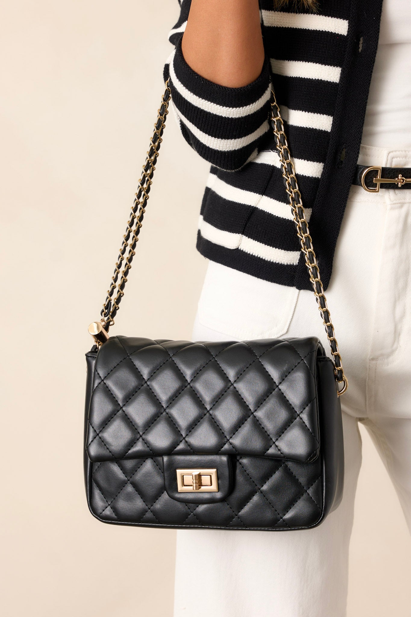 This black bag features gold hardware, a quilted texture, a twist lock closure, a zipper pocket inside, and an adjustable chain strap.