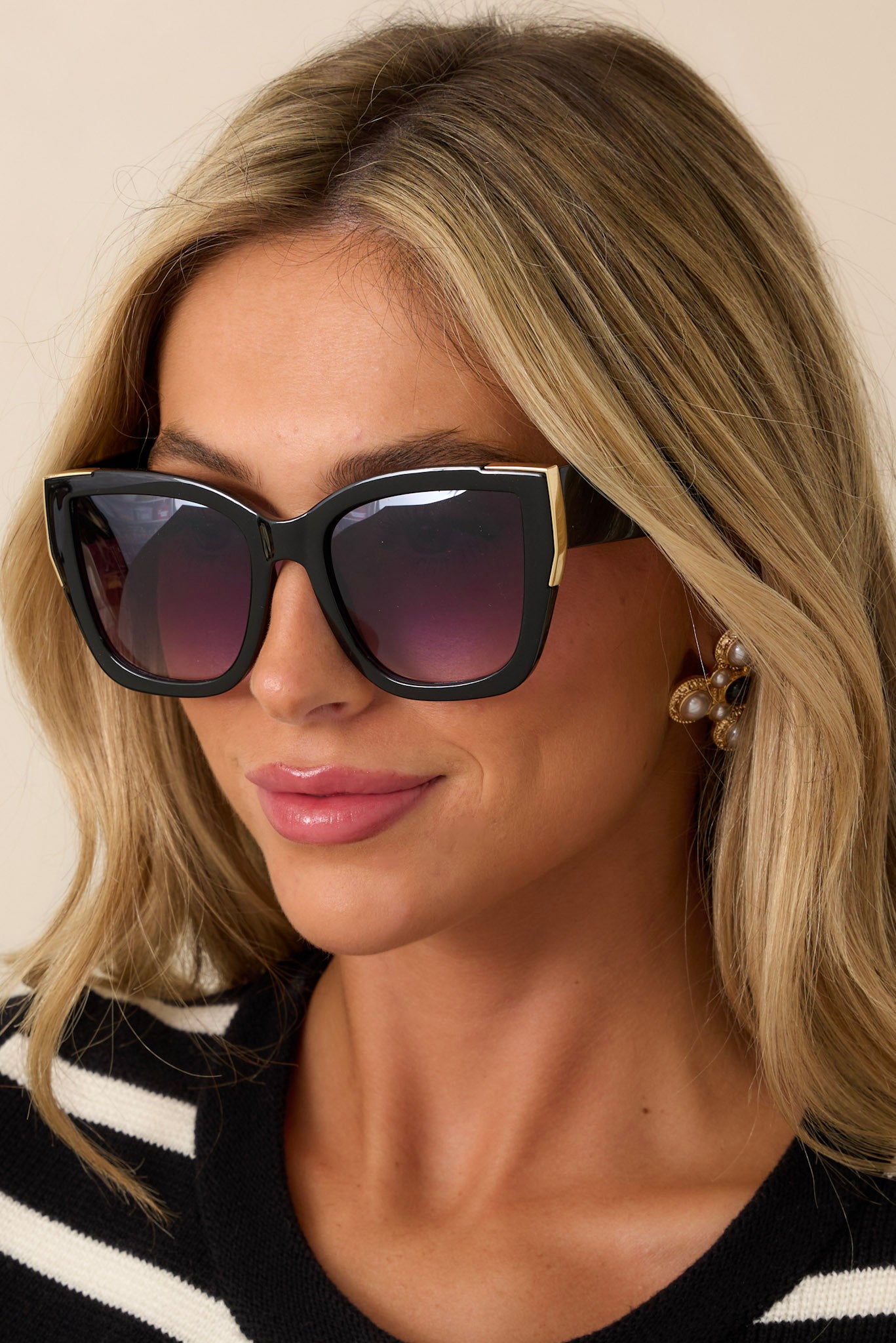 These black sunglasses feature a cat-eye shape, a color fade lens, and gold detailing around the frame.