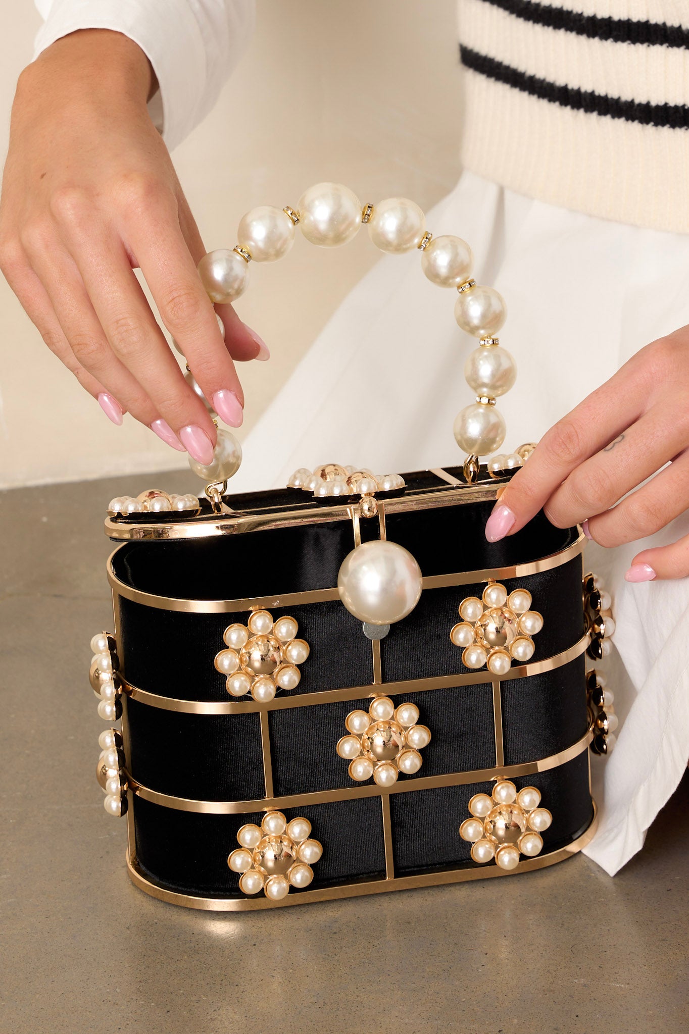 Close up of this faux pearl clutch featuring a box structured shape, adorned with clusters of faux pearls arranged in floral patterns and a large faux pearl handle.