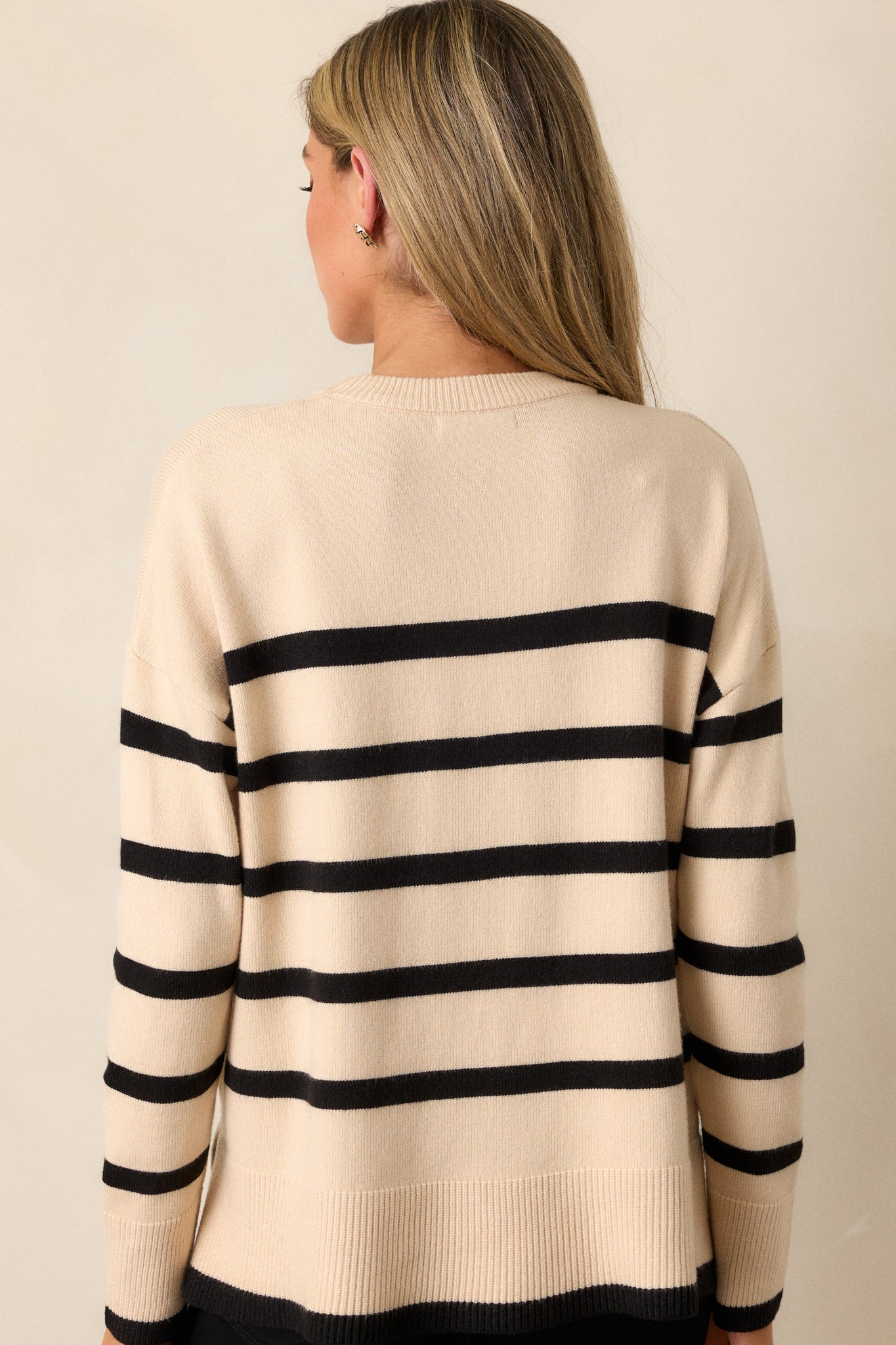 Rear view of the beige sweater, highlighting the ribbed hems, long sleeves, and the horizontal stripe pattern across the back.