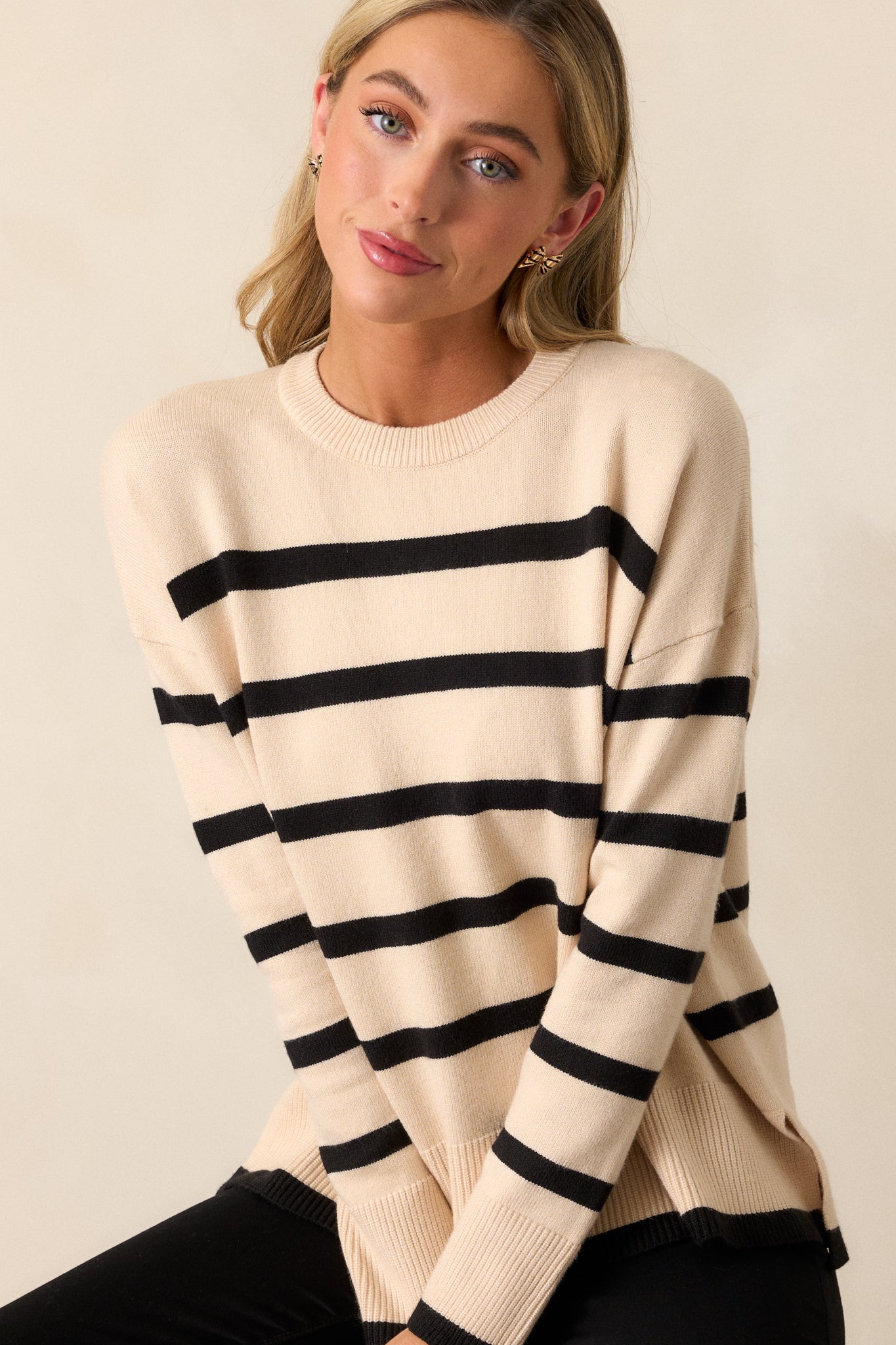 Close-up shot focusing on the long sleeve and ribbed cuff of the beige sweater, showing part of the stripe detail.