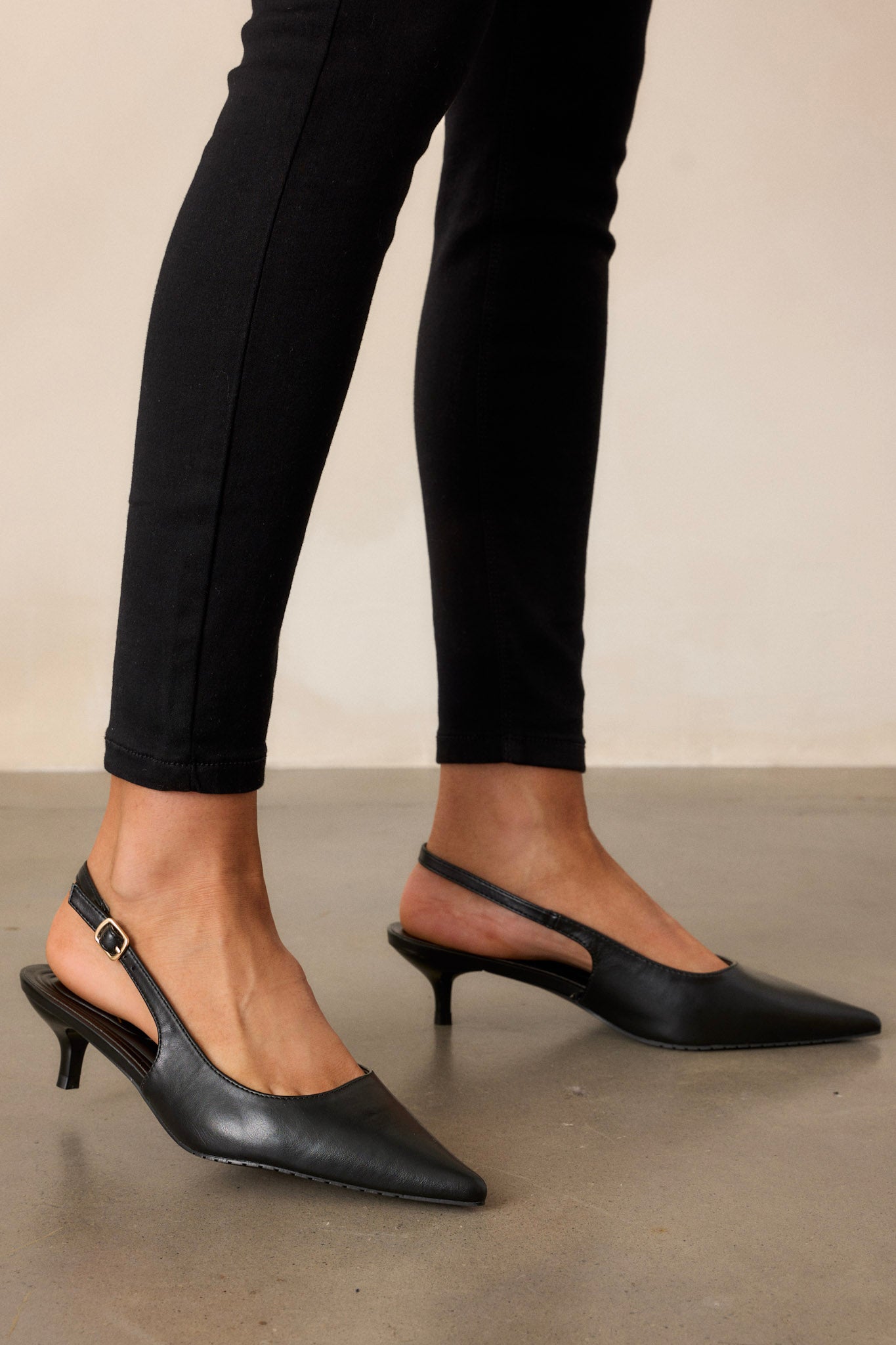 These black heels feature a pointed-toe, a patent material, an adjustable slingback strap with a gold buckle, a short kitten heel, and extra cushioning throughout the shoe.