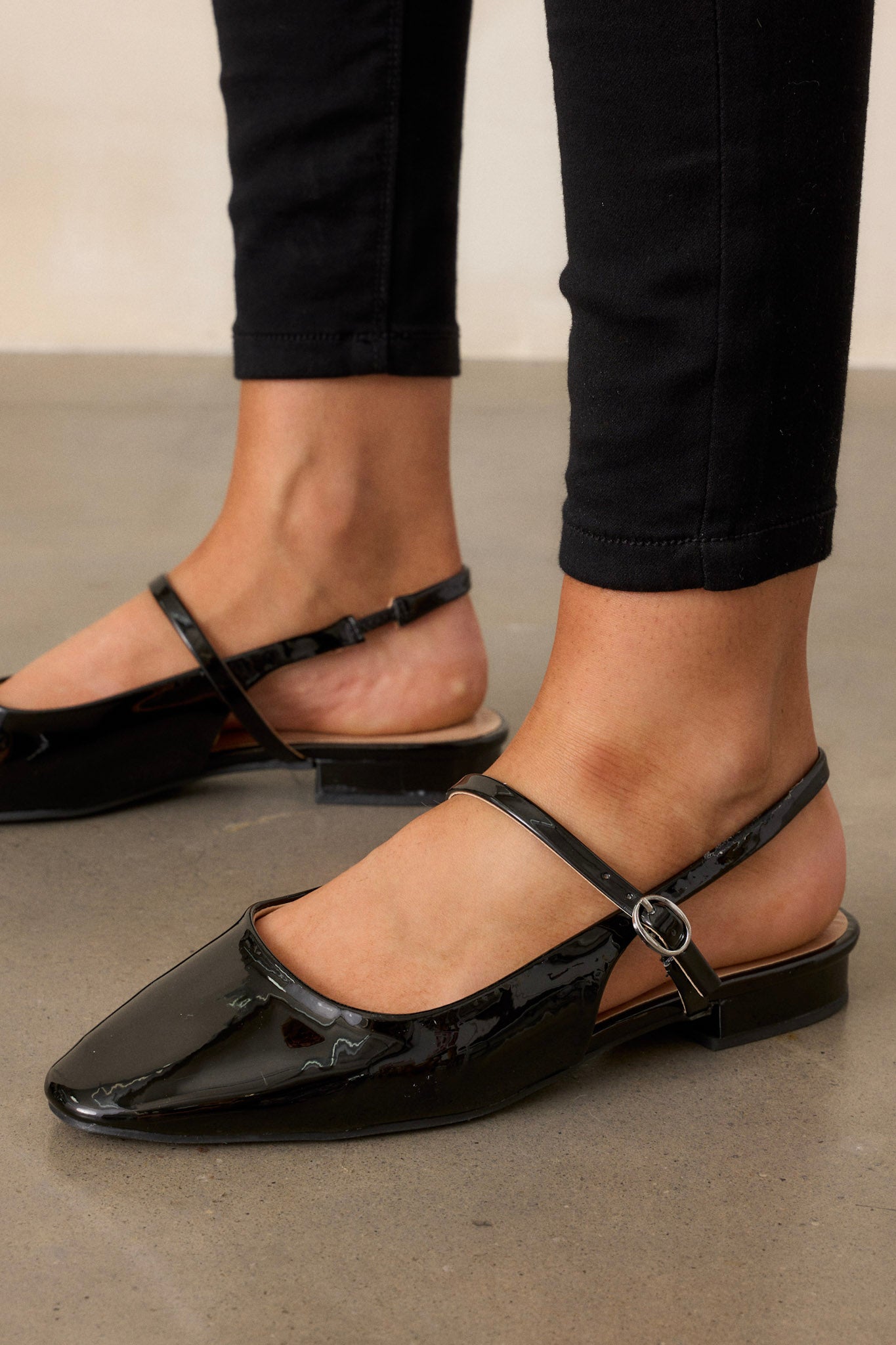 These black flats feature a slightly squared toe, an across the foot strap with a silver buckle, an ankle strap, a small platform, and a shiny black finish.