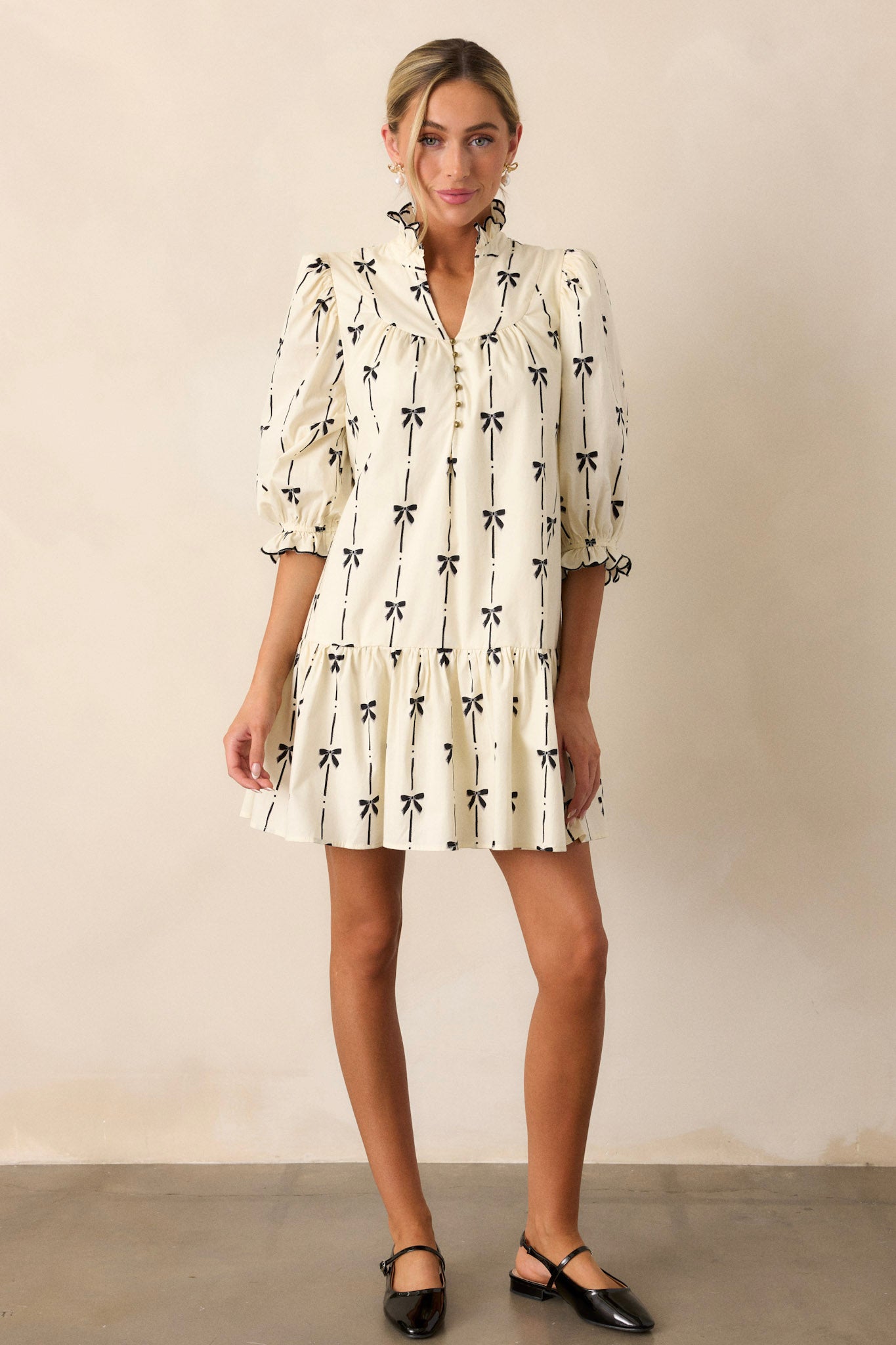 Full-length view of the ivory dress, highlighting the ruffle v-neckline, black bow print, and functional hip pockets on each side.