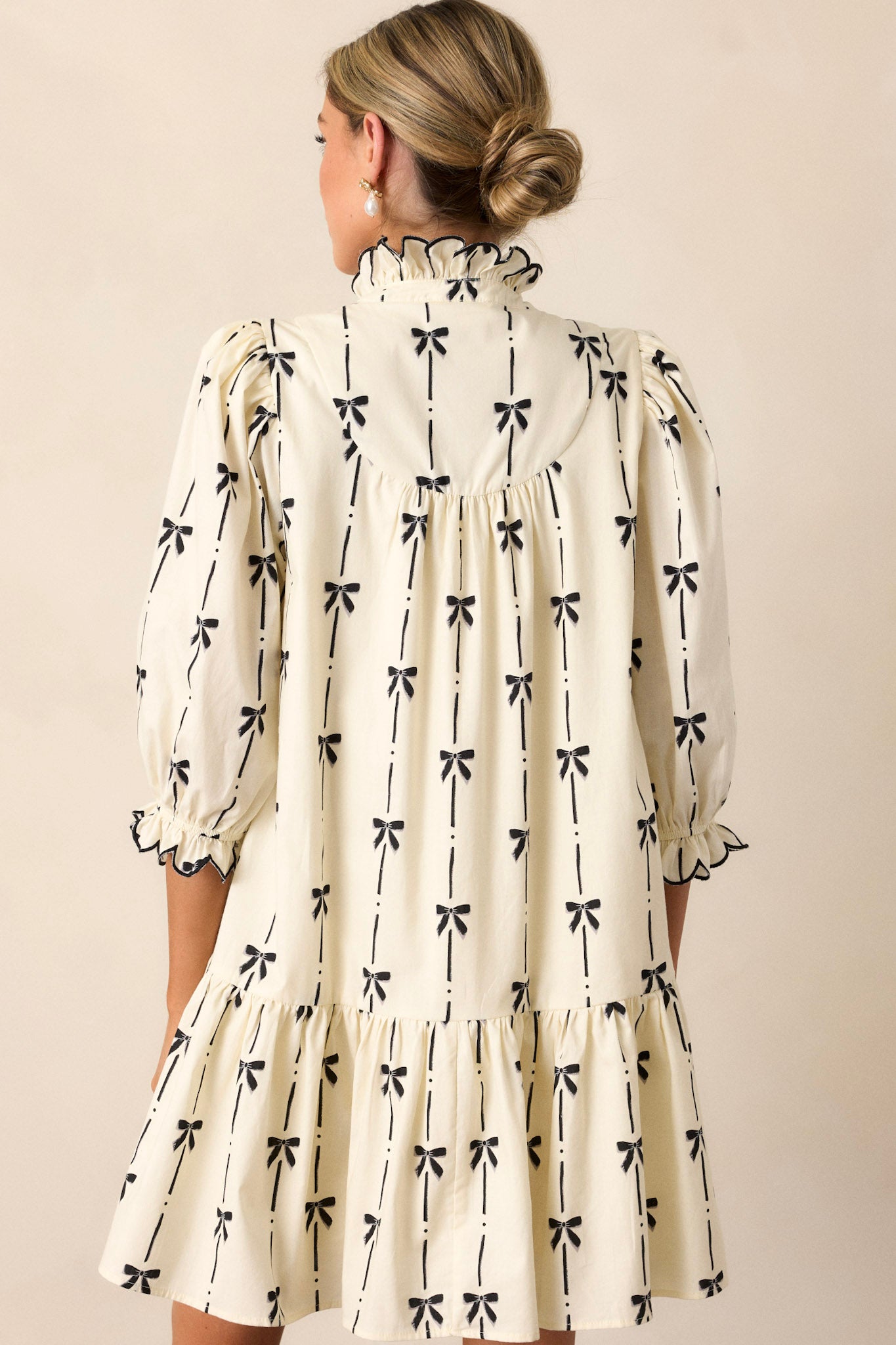 A view of the back of the ivory dress, highlighting the continuation of the black bow print and the clean lines of the ruffle v-neckline and three-quarter length sleeves.