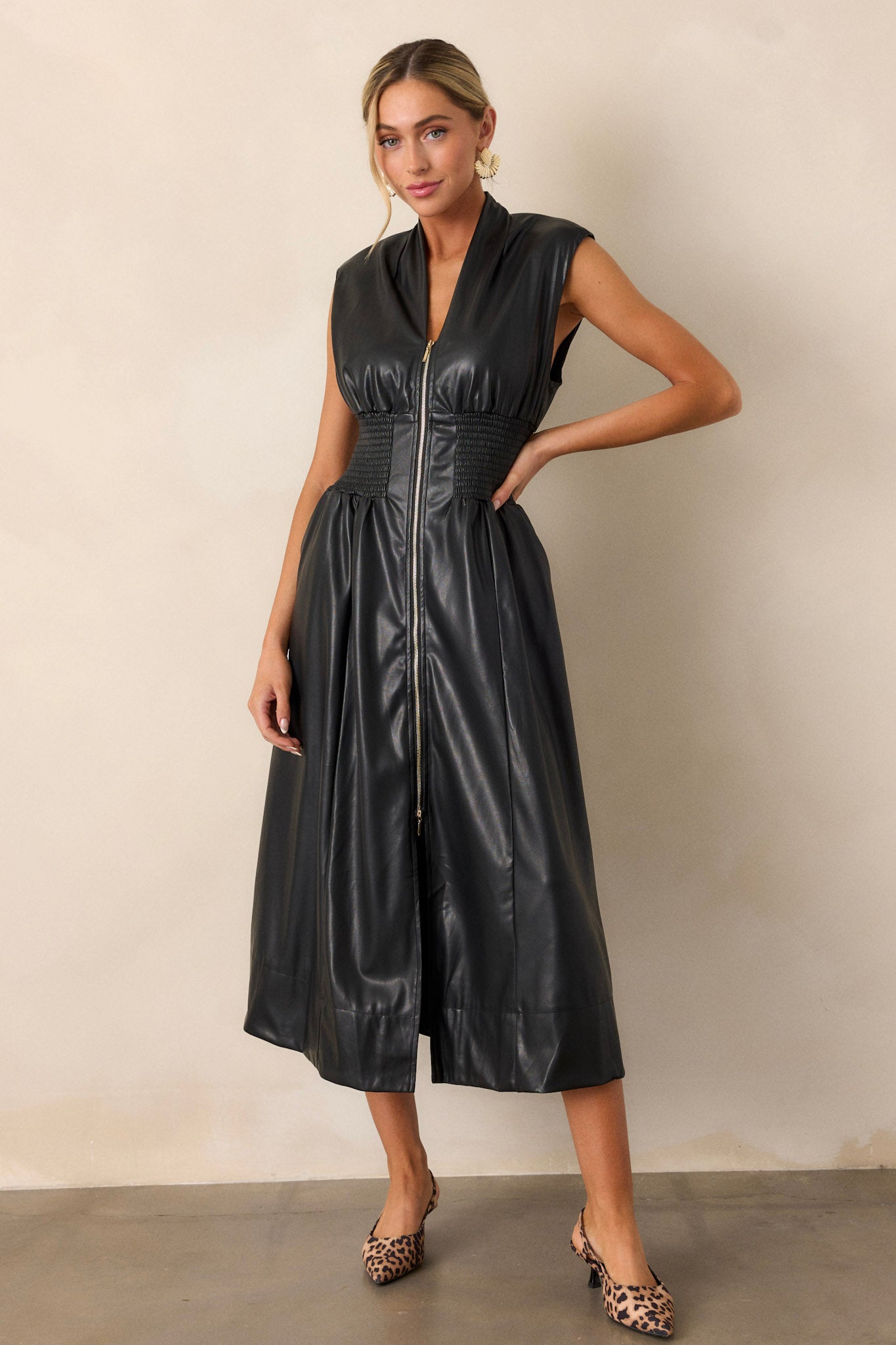 Full-length shot focusing on the dress’s structured padded shoulders, sleek faux leather texture, and the bold gold zipper detailing.