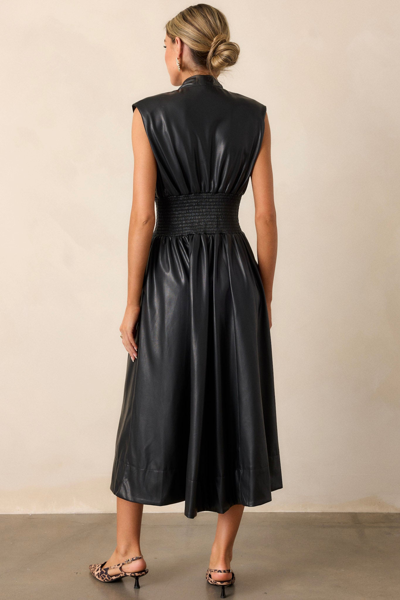 Back view of the black faux leather midi dress, displaying the smooth finish of the material, padded shoulder structure, and the clean, continuous line down the back.





