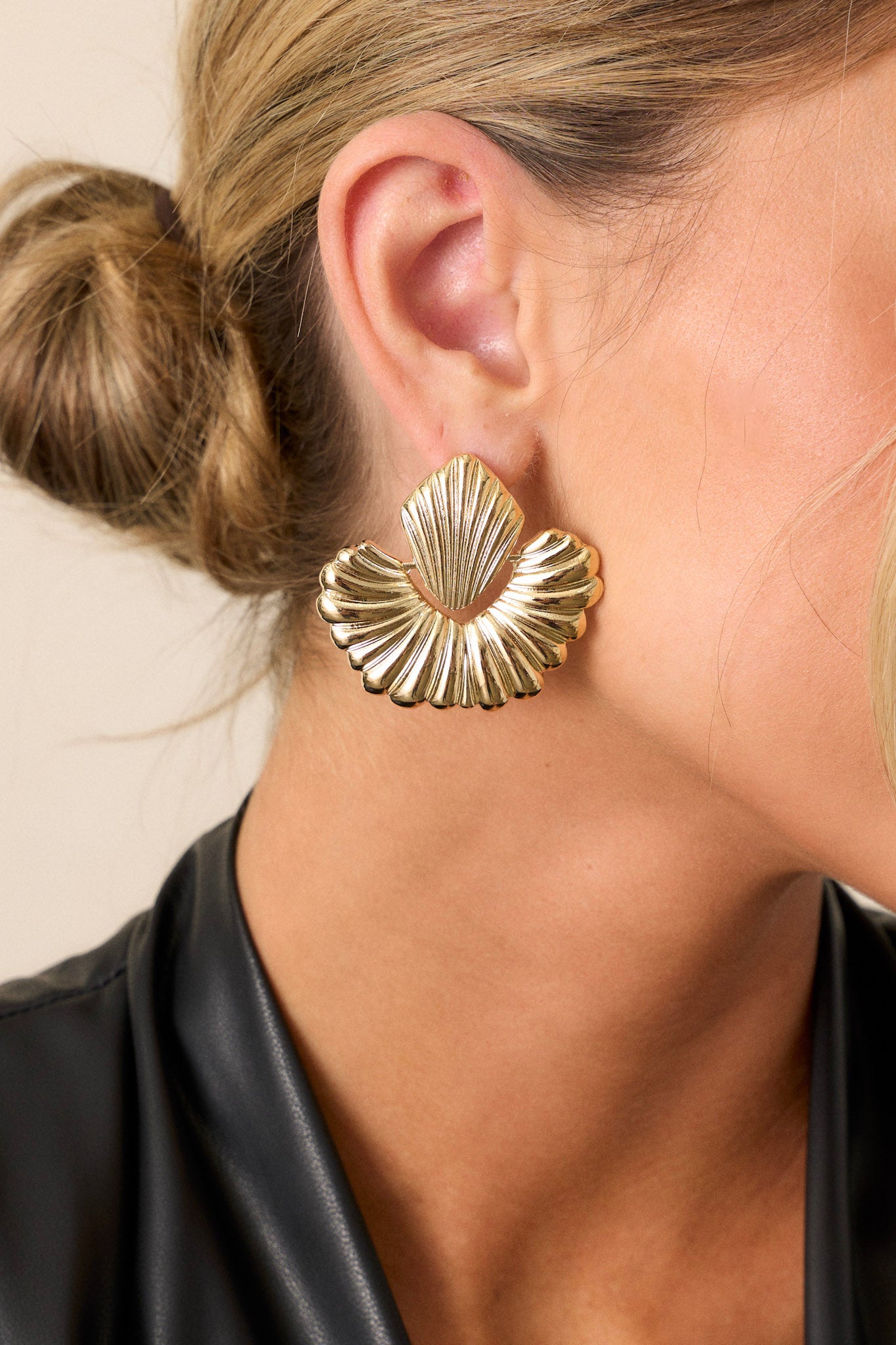 A pair of gold earrings showcasing textured gold hardware, featuring a textured rhombus stud connected to a semi-circle hoop, displayed against a plain background.