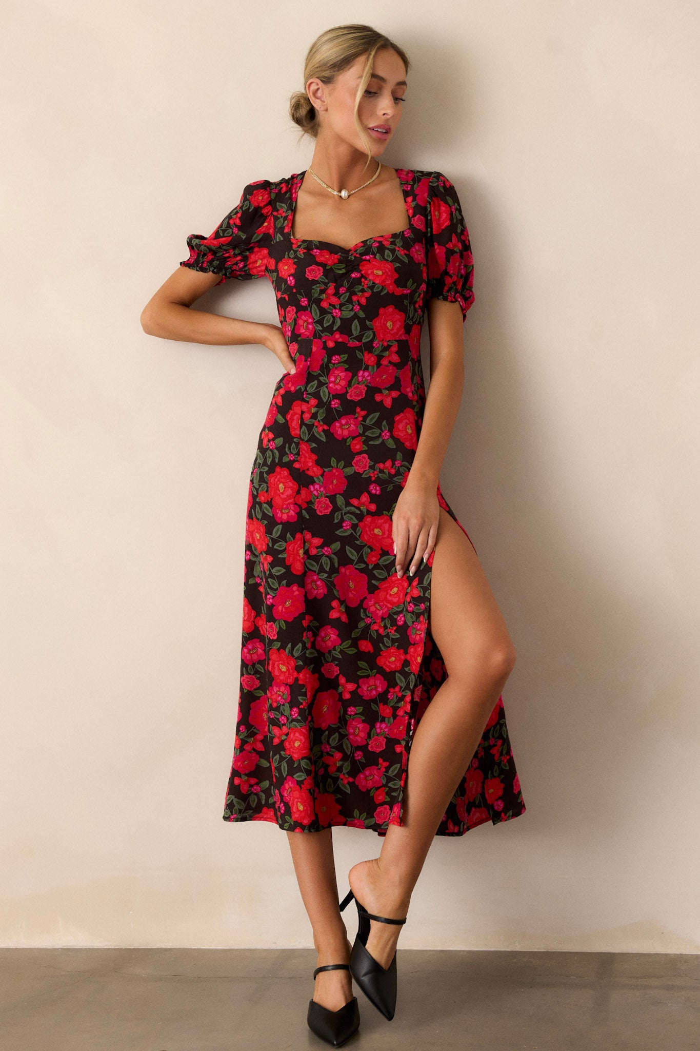 A full-length view of the black floral dress featuring a square neckline and short elastic cuffed puff sleeves, showcasing the vibrant pink and red floral print.