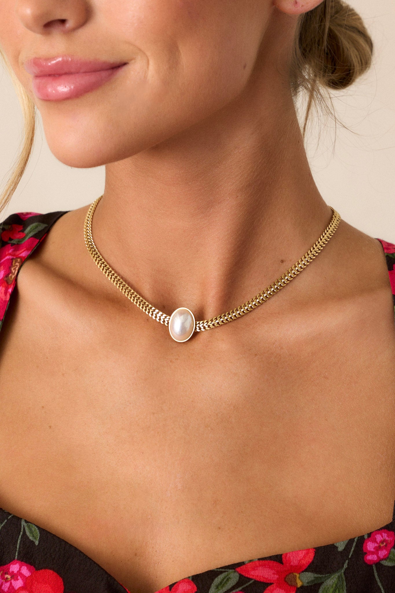 This gold necklace features a double curb chain, and an oval bezel-set faux pearl centerpiece.