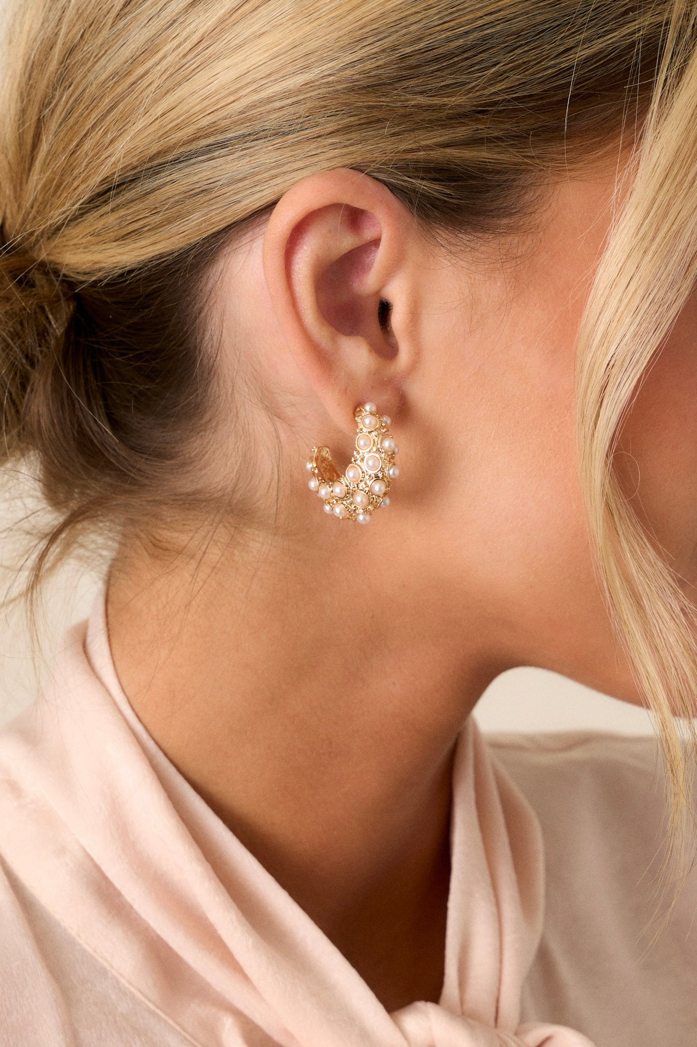 A pair of gold earrings featuring an incomplete hoop design adorned with small gold dots for added depth and medium faux ivory pearls, showcased against a simple background.