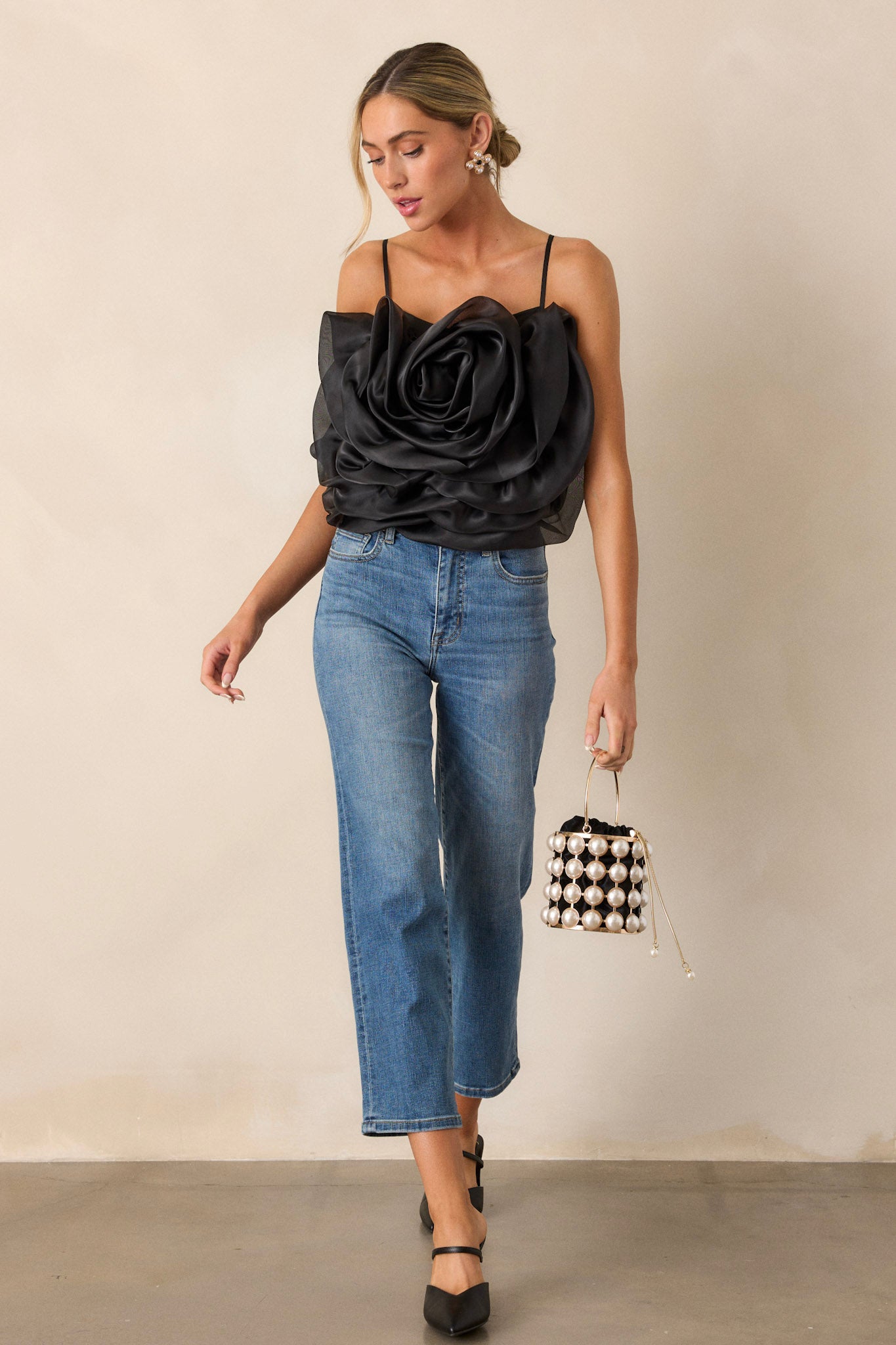 Front view of a black crop top featuring a square neckline, thin and stretchy adjustable straps, a fully smocked back, a large 3-D flower, and a cropped hemline