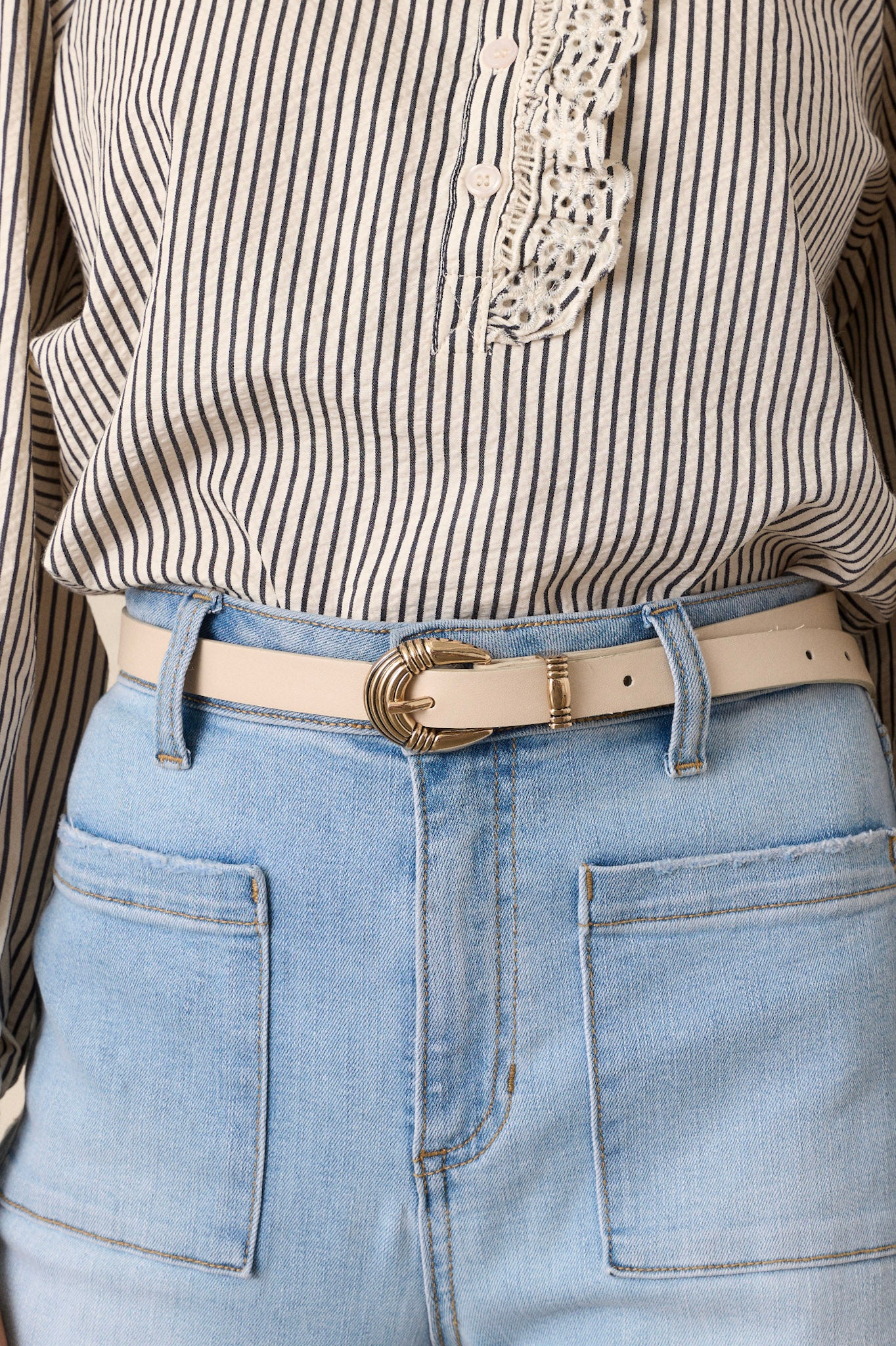 Close-up view of this ivory belt featuring gold hardware, a pin buckle, and a faux leather material.