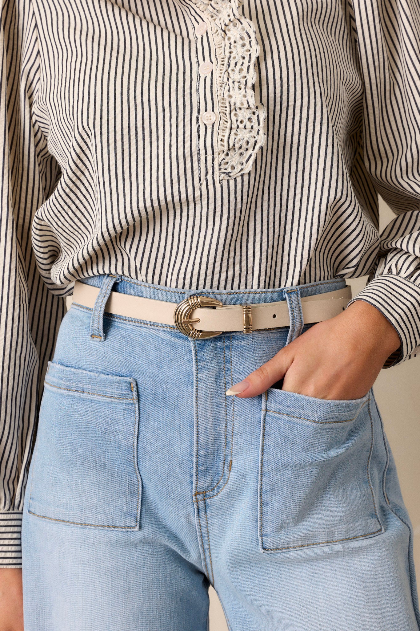 This ivory belt features gold hardware, a pin buckle, and a faux leather material.