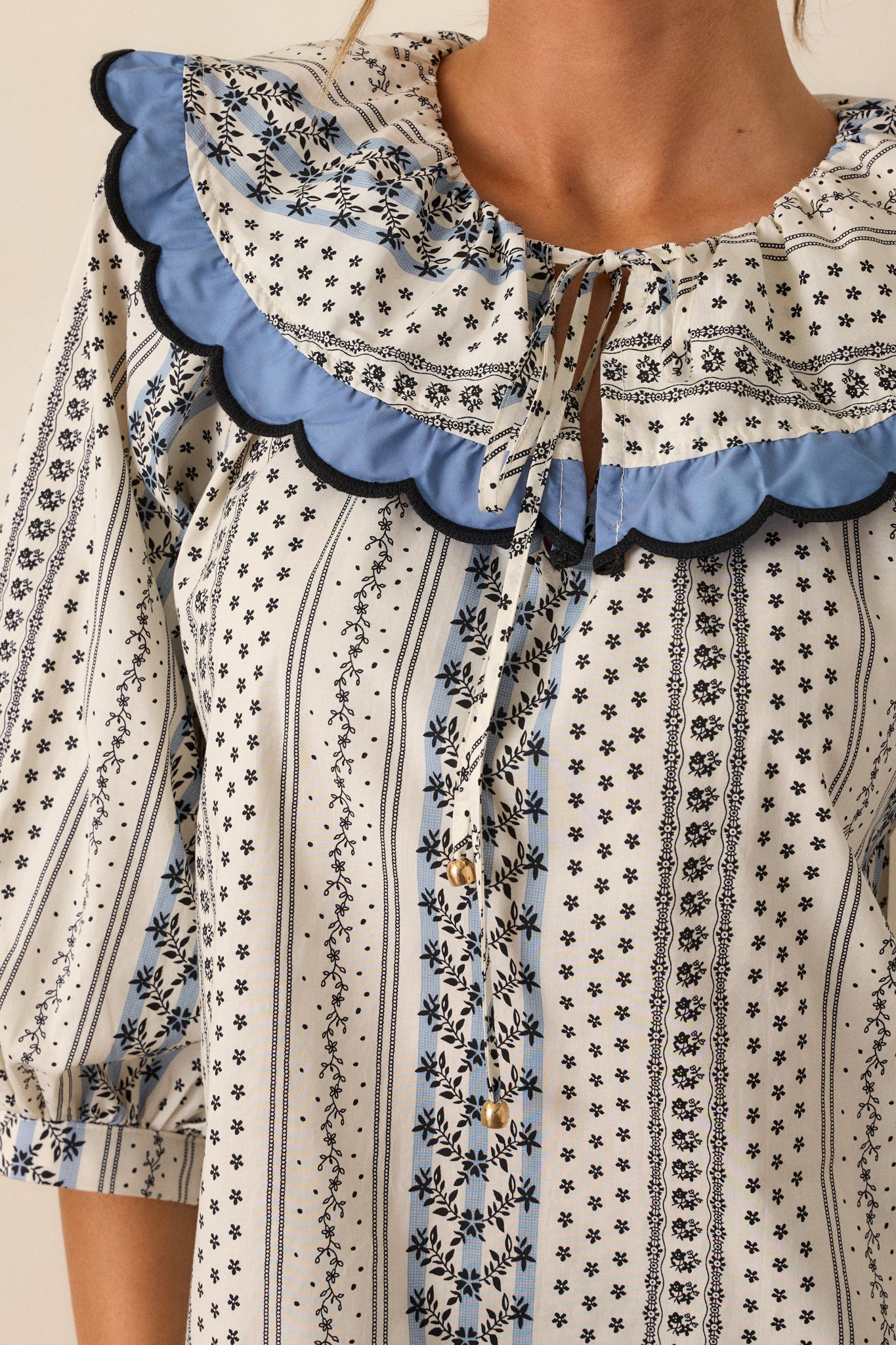 Close-up of the floral stripe print on the ivory top, emphasizing the texture and fine details of the scallop collar and cuffs.