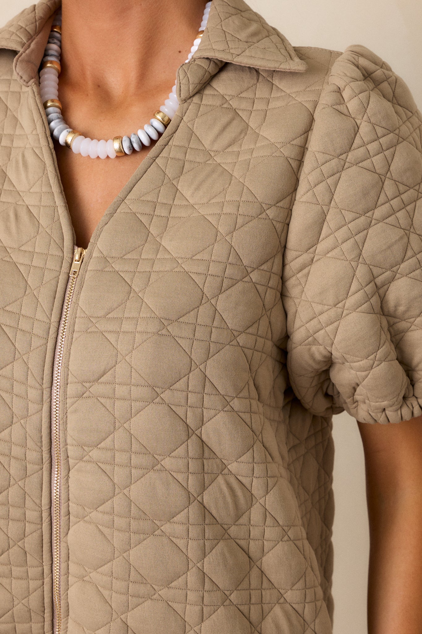 A close-up of the quilted fabric of the tan dress, focusing on the fine texture and the functional full-zip detail.