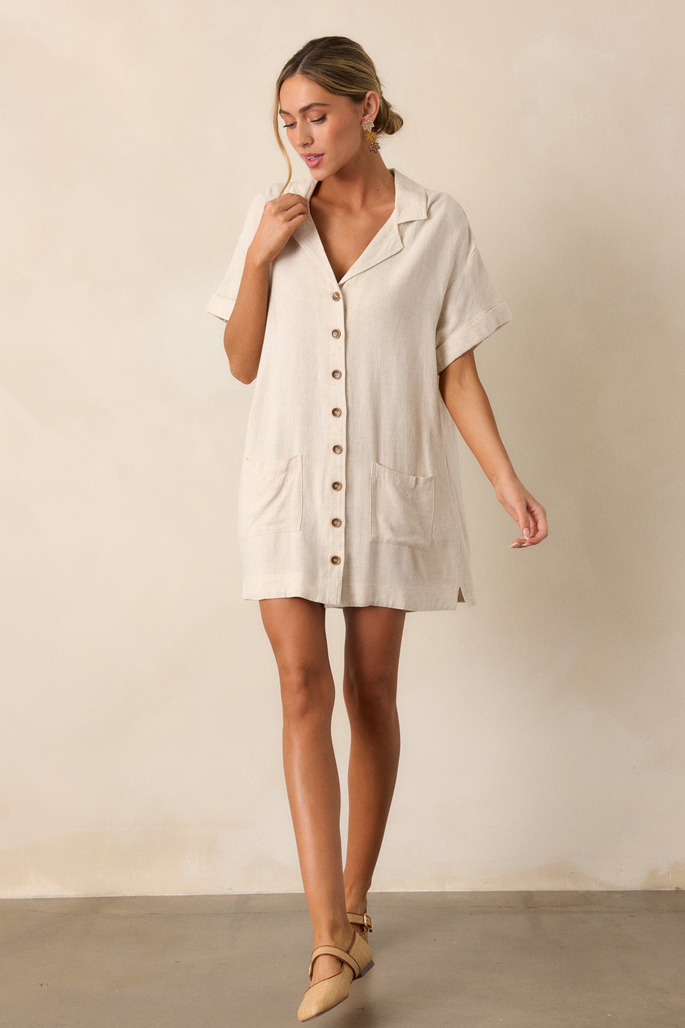 A full view of the beige mini dress, highlighting the collared v-neckline, relaxed fit, and functional button front.