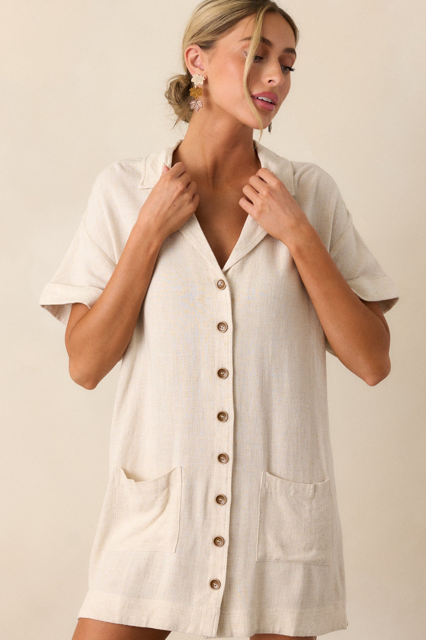 Close-up of the neckline and upper buttons, showcasing the collared v-neckline and the smooth beige fabric.