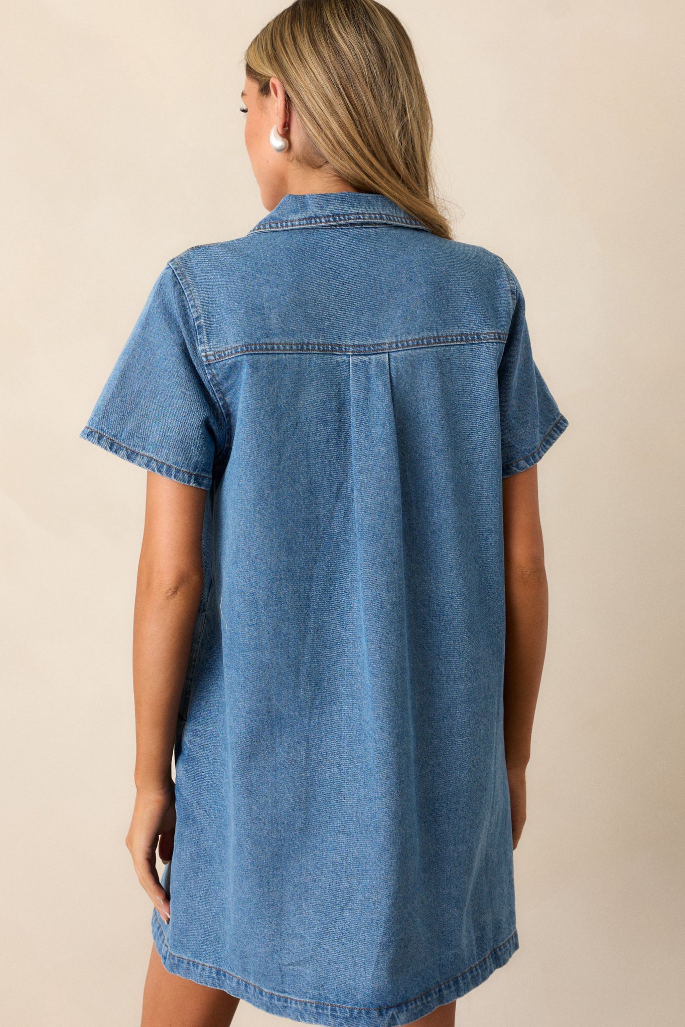 Back view of the denim mini dress, displaying the collar and the clean lines of the denim material from behind.





