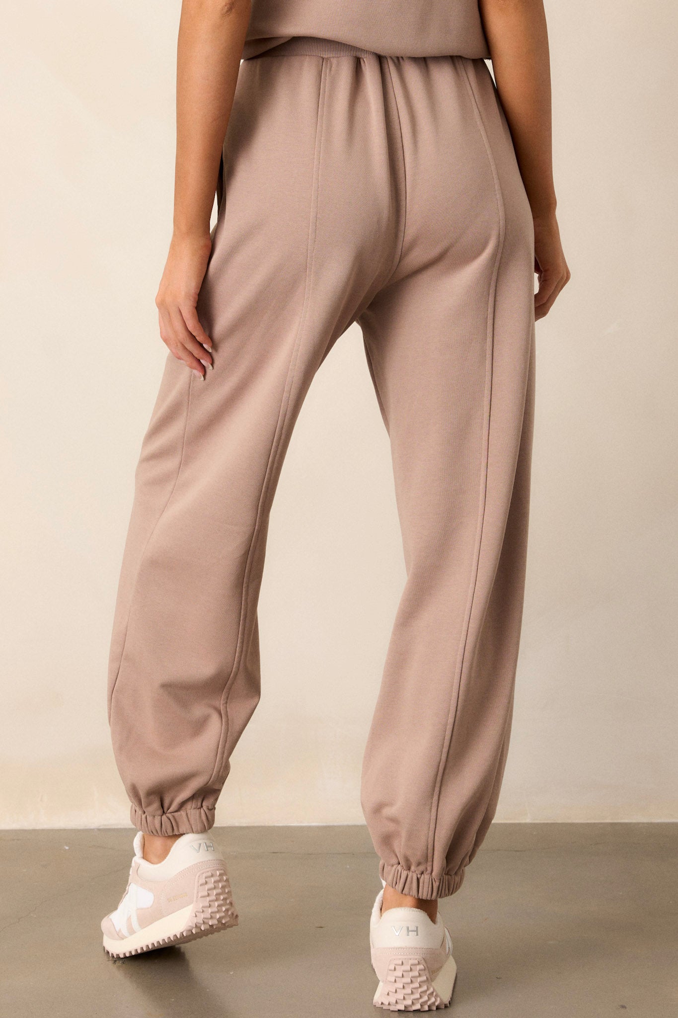 Back view of these light mocha joggers that feature a thick elastic waistband, an optional waist drawstring, functional hip pockets, a soft fabric, and elastic cuffed ankles.