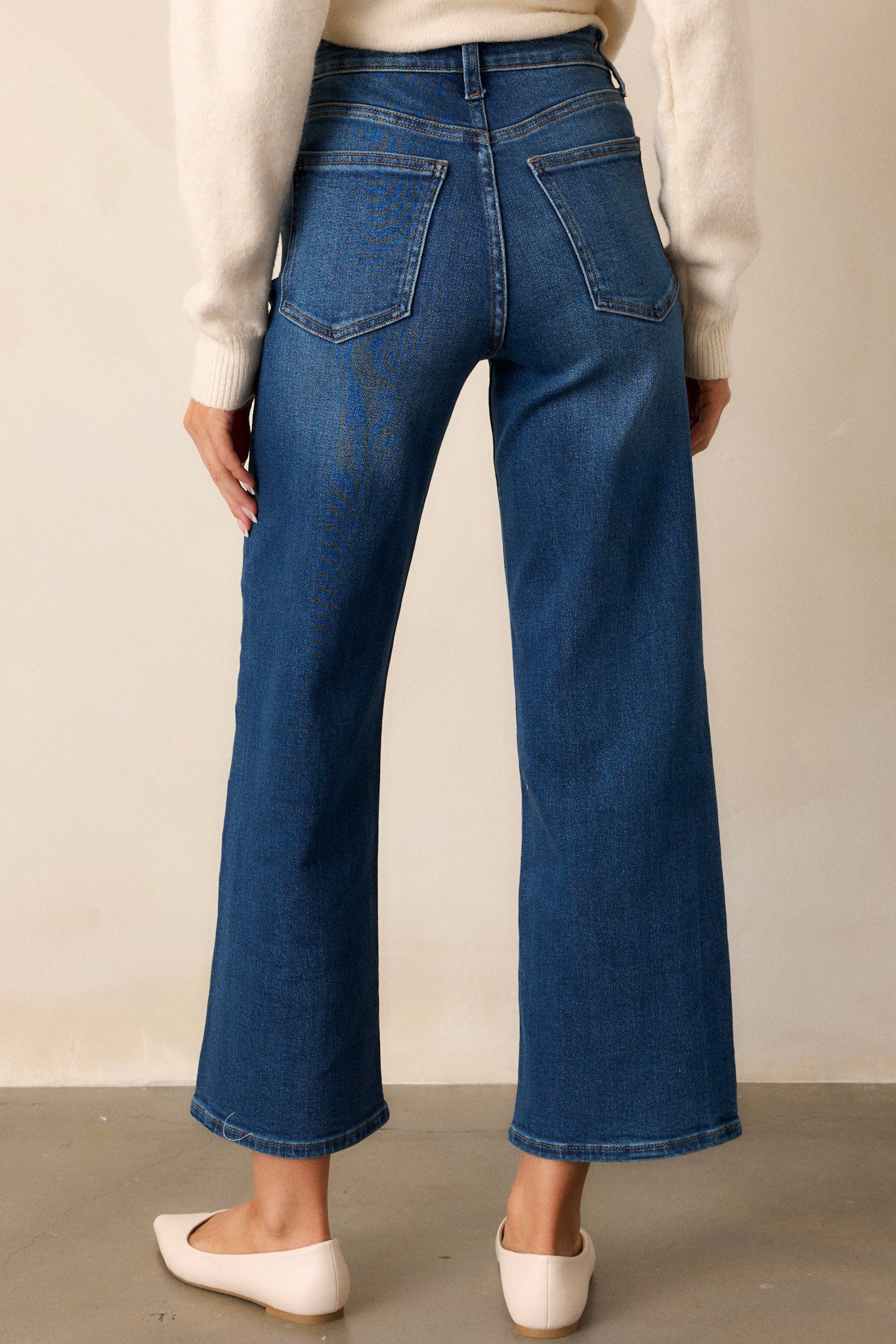 Back view of dark wash jeans featuring a high waisted design, classic button & zipper closure, belt loops, functional front & back pockets, and a cropped length.