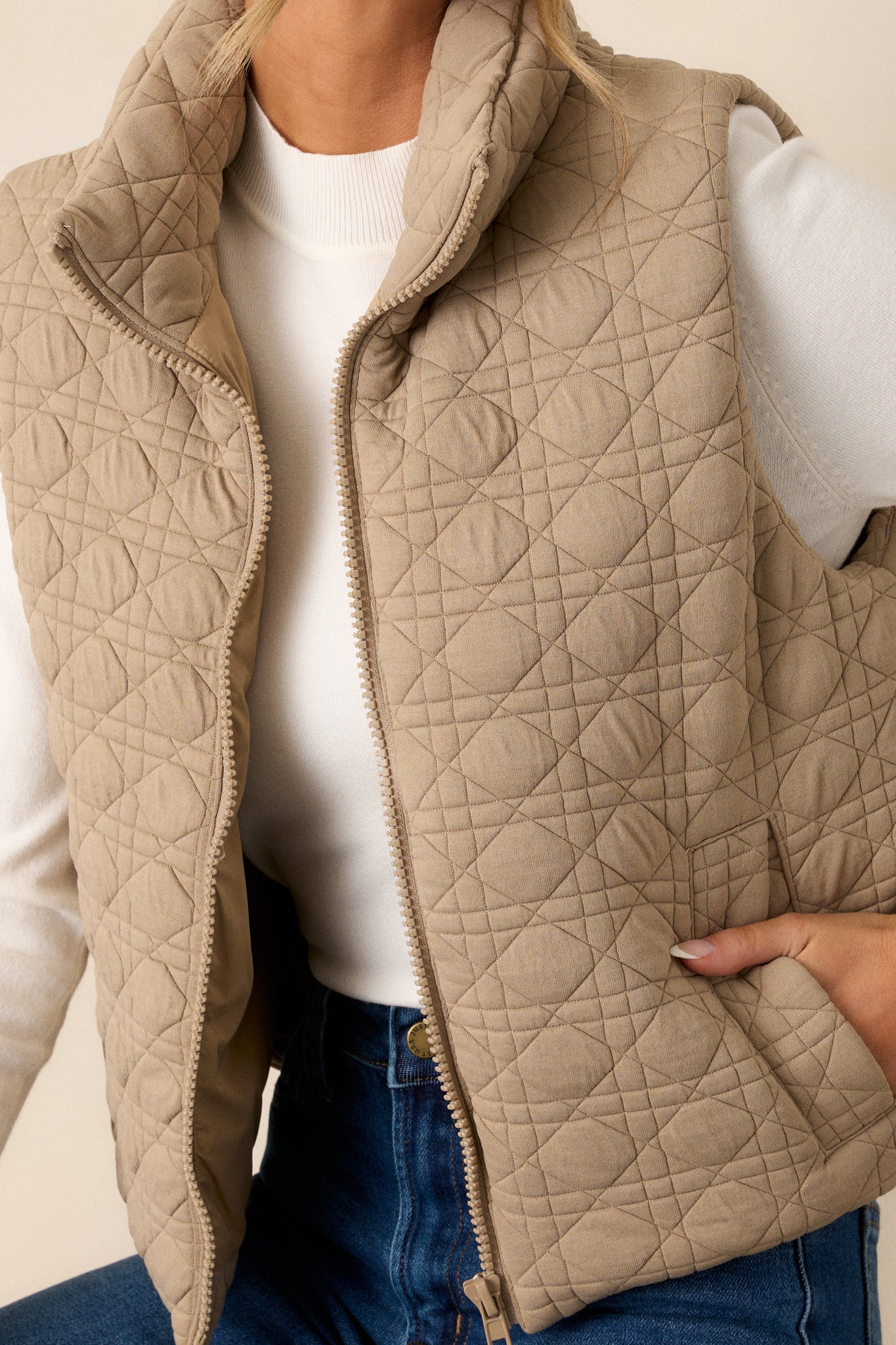 Close up on the collar and quilted fabric of this tan zip-up vest. 