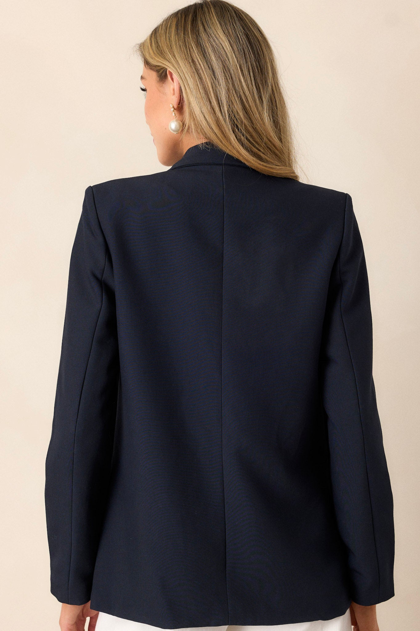 Back view of a navy blazer highlighting the padded shoulders, long sleeves, and the overall fit.