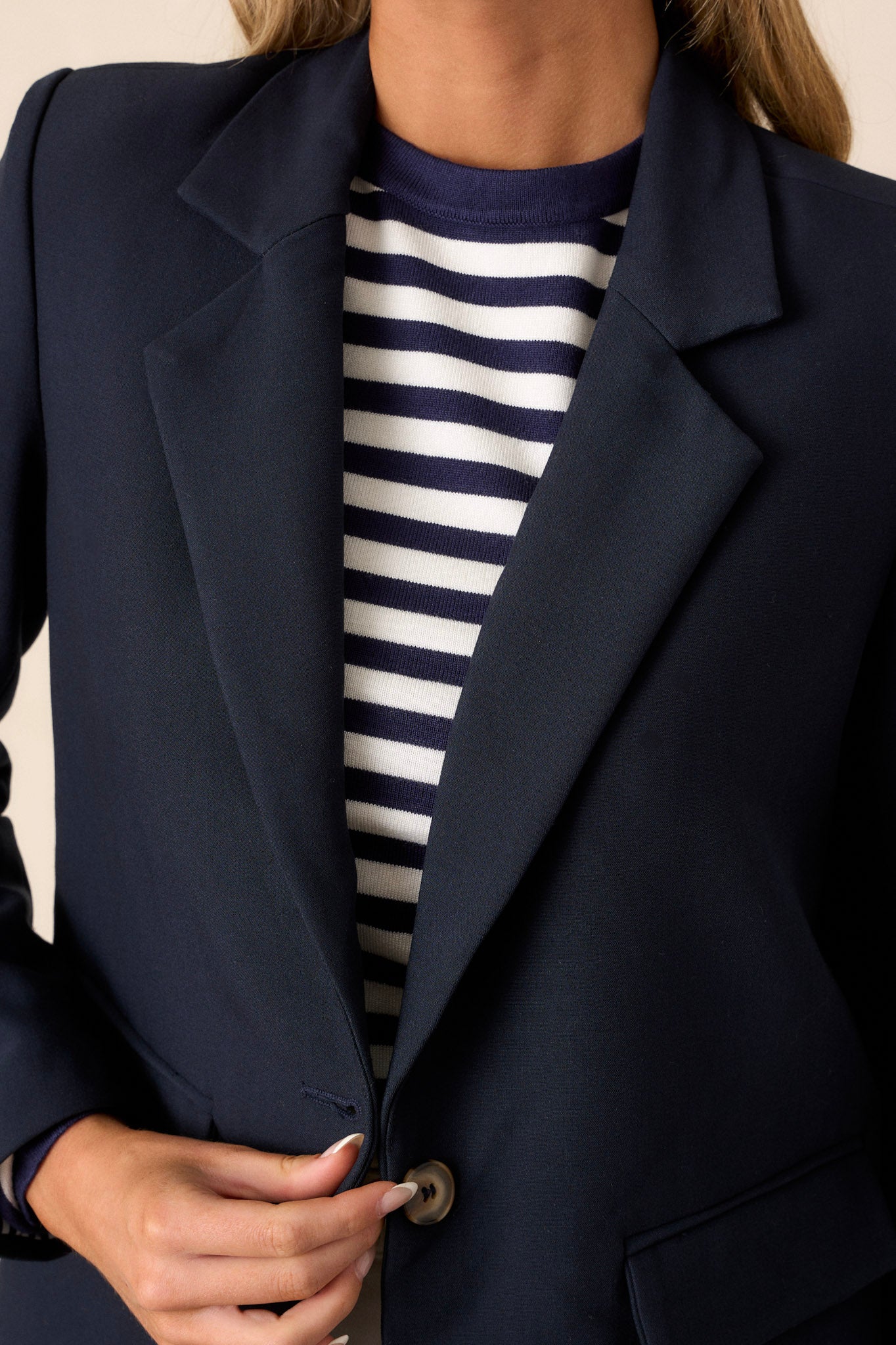 Close-up of a navy blazer showing the collared neckline, middle button closure, floral lining, and padded shoulders.