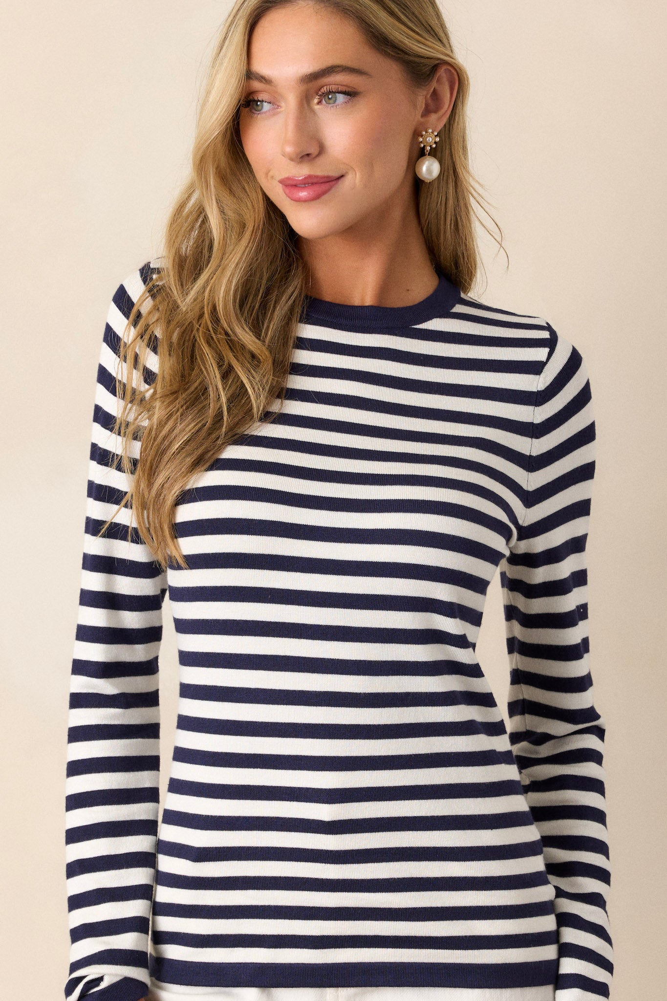 Full view of an ivory top featuring a crew neckline, long sleeves, a navy stripe pattern, a light weight fabric, and a close fit.