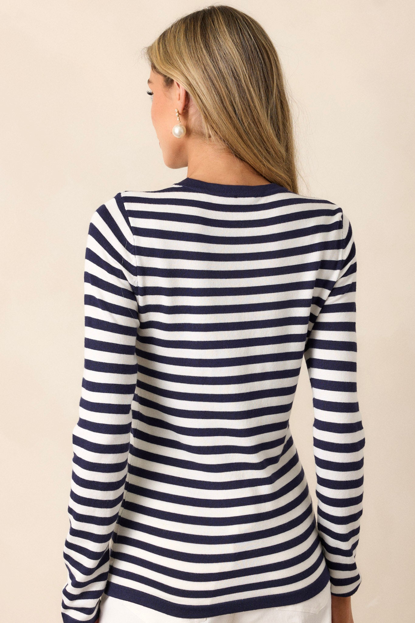 Back view of an ivory top featuring a crew neckline, long sleeves, a navy stripe pattern, a light weight fabric, and a close fit.