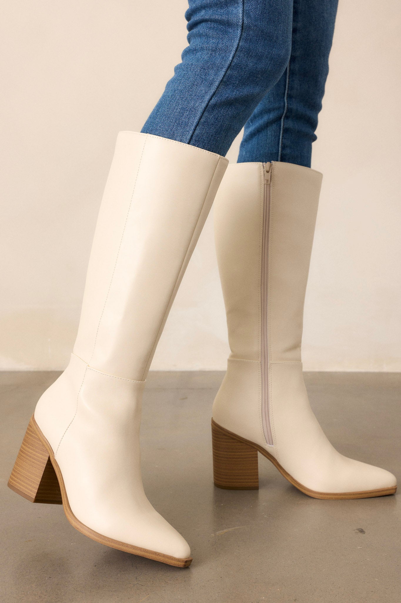 These ivory boots feature a pointed toe, a sleek faux leather ivory material, a brown block heel, a functional side zipper, a knee high design and a brown sole.