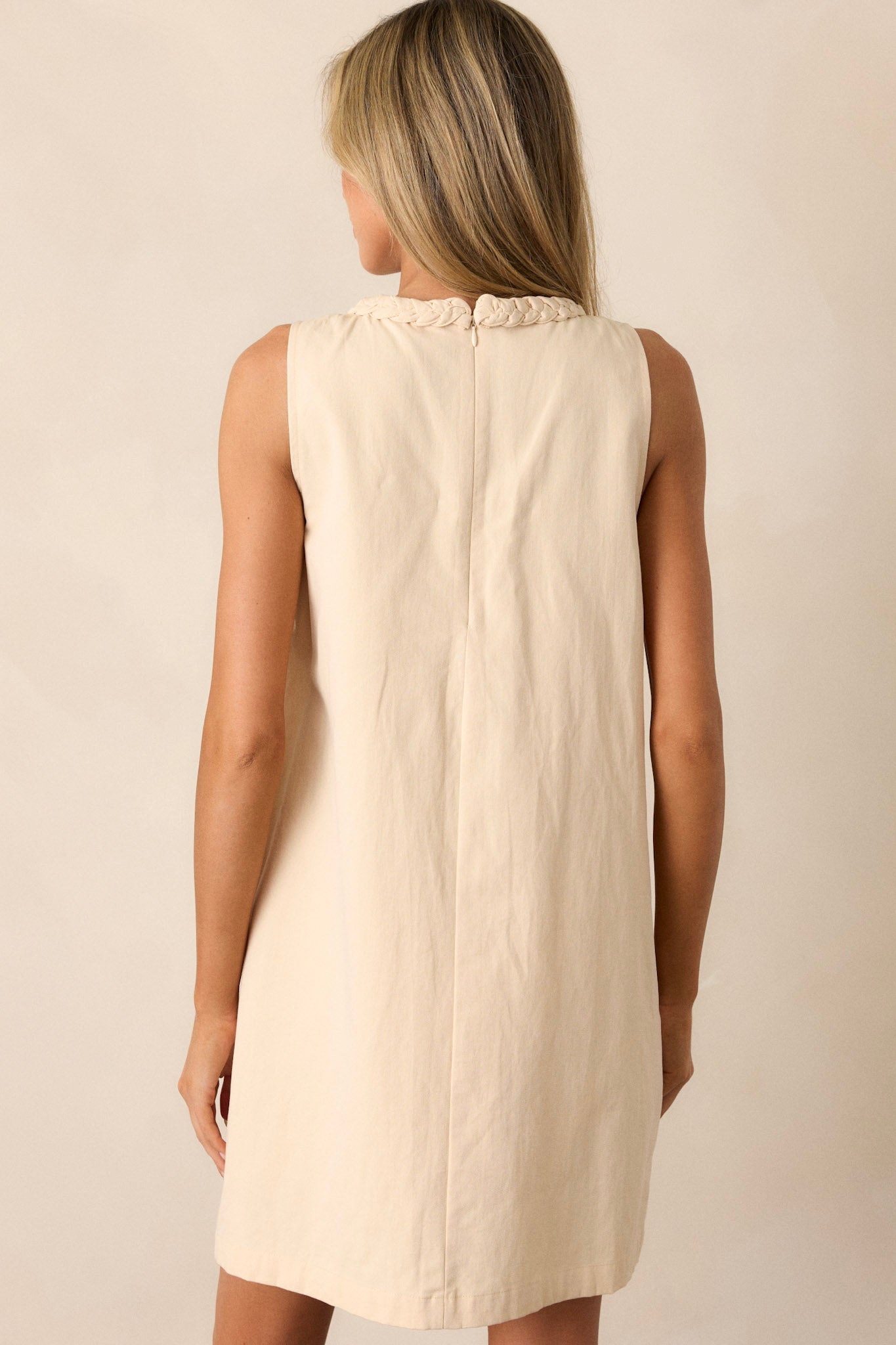 Back view of a light beige dress highlighting the discrete zipper, braided detailing, and overall fit.